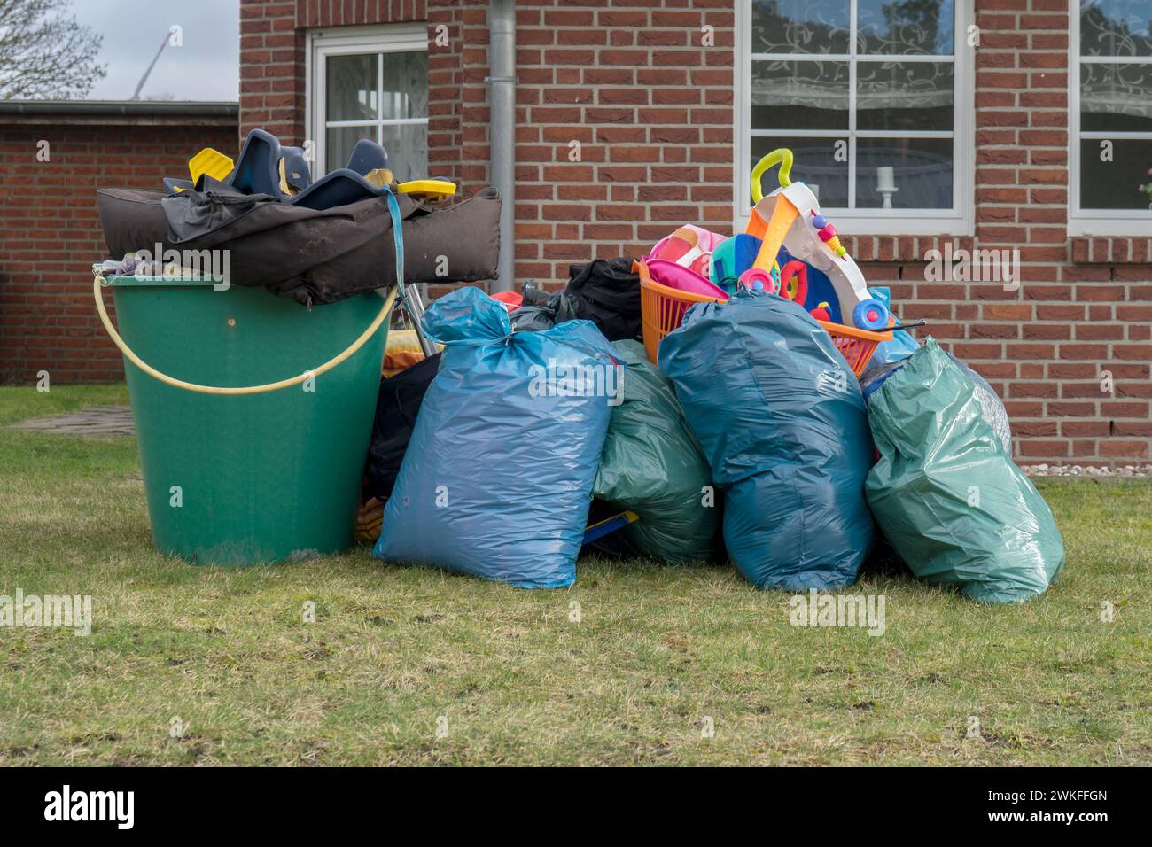 Pile de déchets encombrants devant une maison avec des sacs à ordures, des barils de pluie et des jouets Banque D'Images