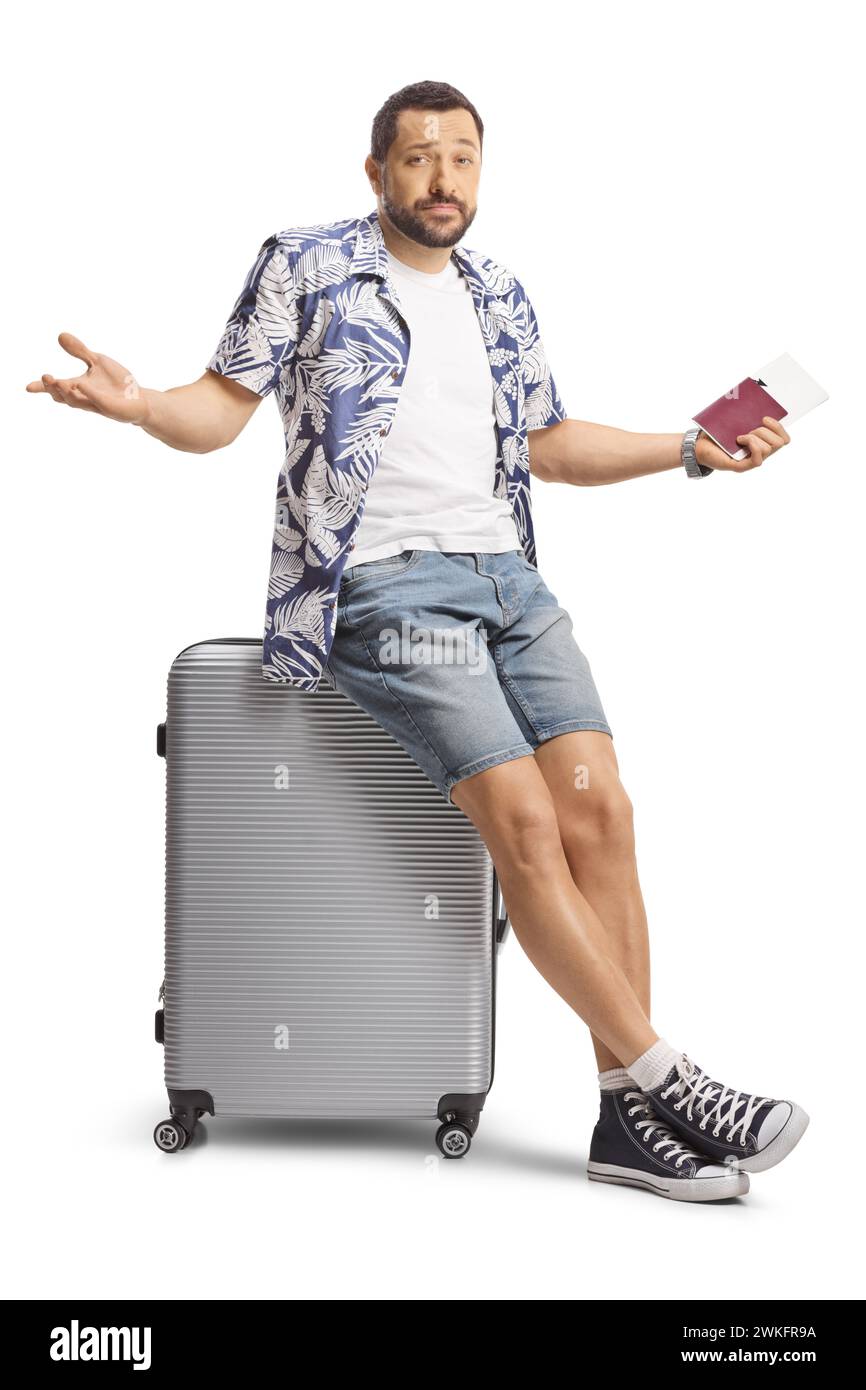 Touriste masculin confus tenant un passeport et assis sur une valise isolé sur fond blanc Banque D'Images