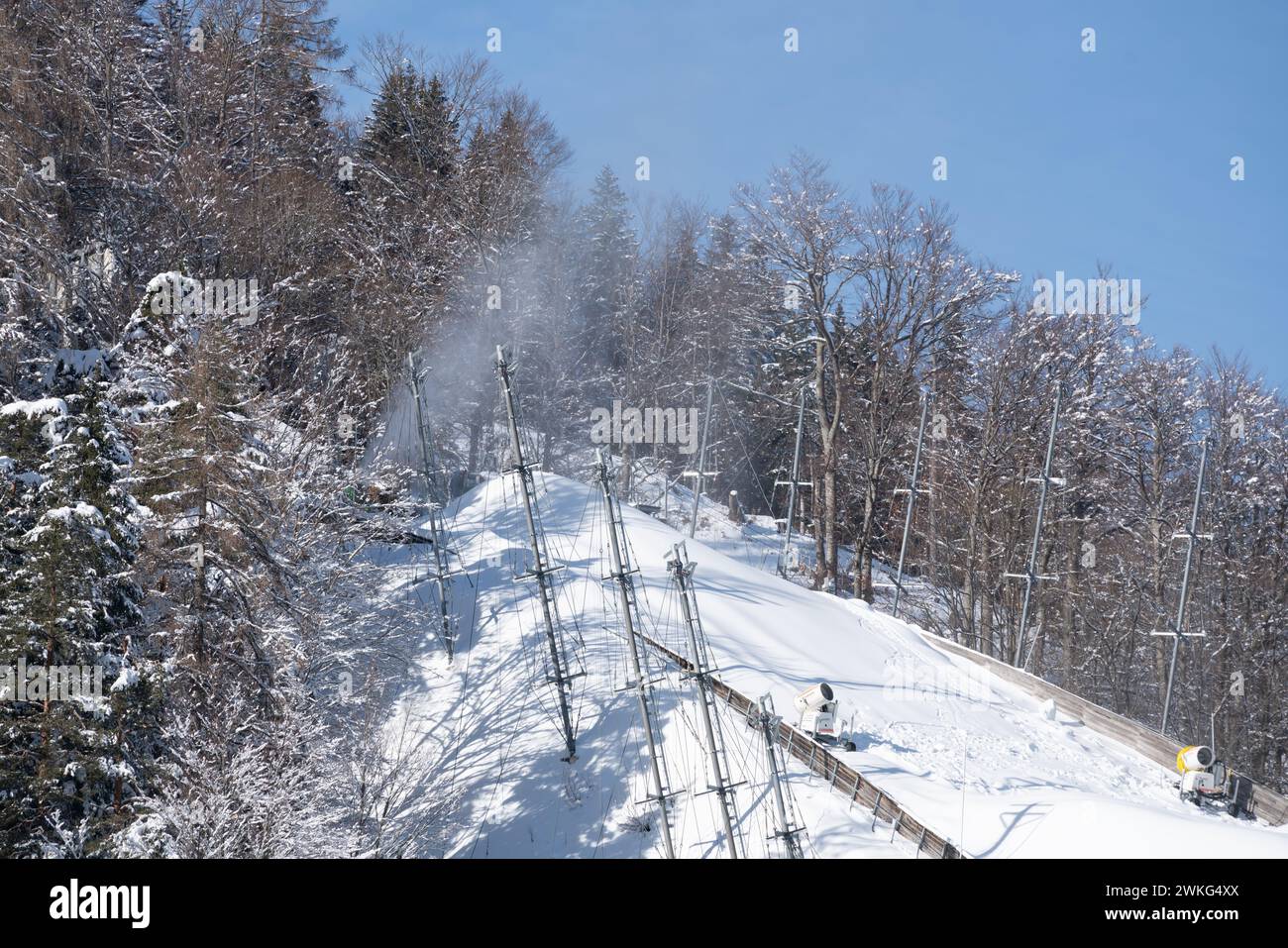 Des pistolets à neige au sommet du saut à ski géant faisant de la neige par une journée ensoleillée, entouré de forêts enneigées à Planica, en Slovénie Banque D'Images