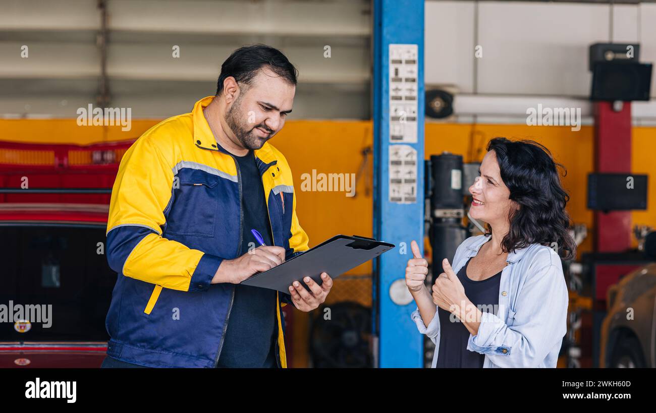 Les femmes clientes heureuses apprécient avec la liste de contrôle de service de voiture de travailleur de mécanicien dans l'atelier de centre d'auto Banque D'Images
