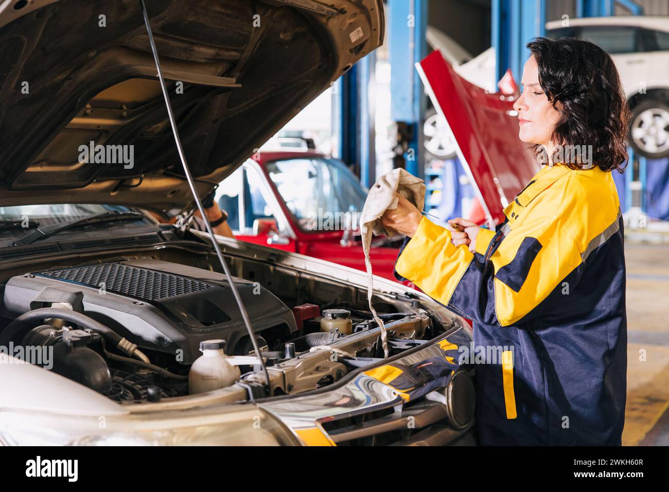 Le travailleur de femmes mécanicien automatique de garage qui travaille vérifie le bâton de niveau d'huile moteur dans le travail professionnel de centre de service de voiture Banque D'Images