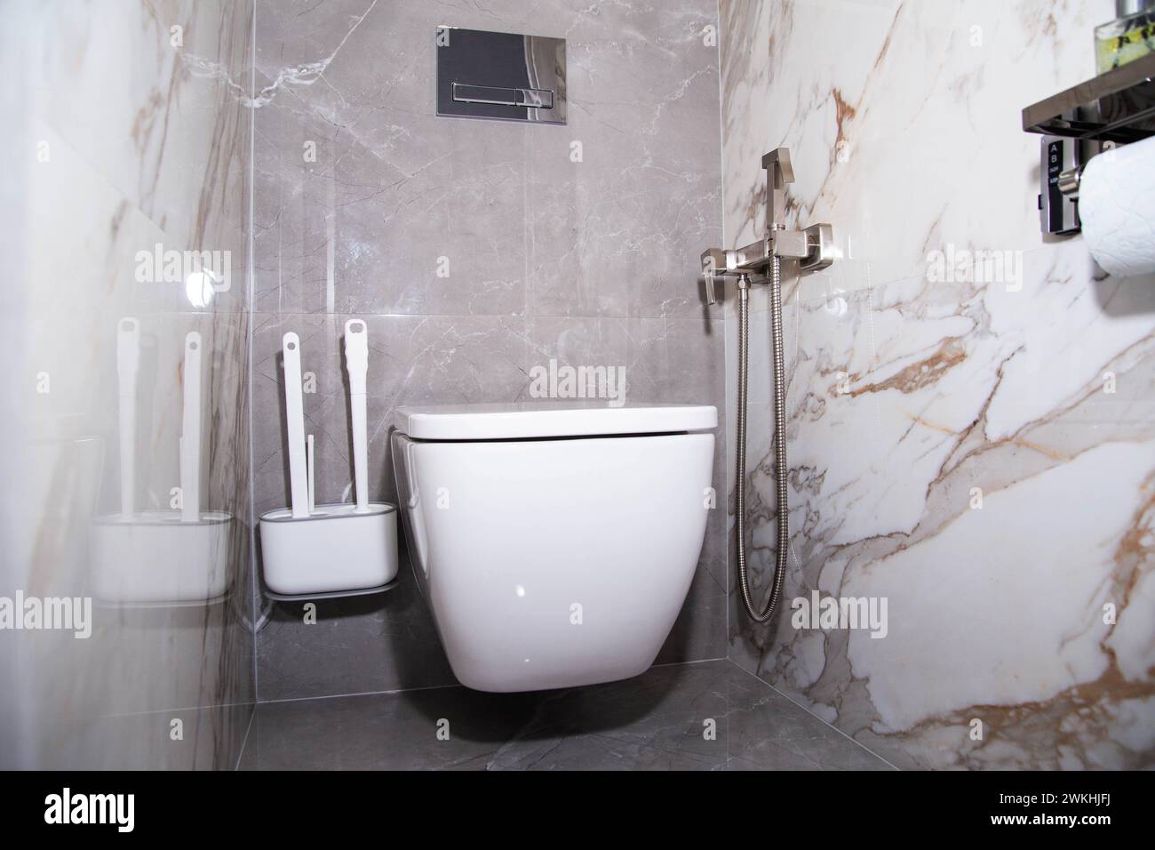 L'intérieur d'une toilette moderne avec des carreaux de porcelaine grise sur les murs, une toilette murale et une douche hygiénique. Banque D'Images