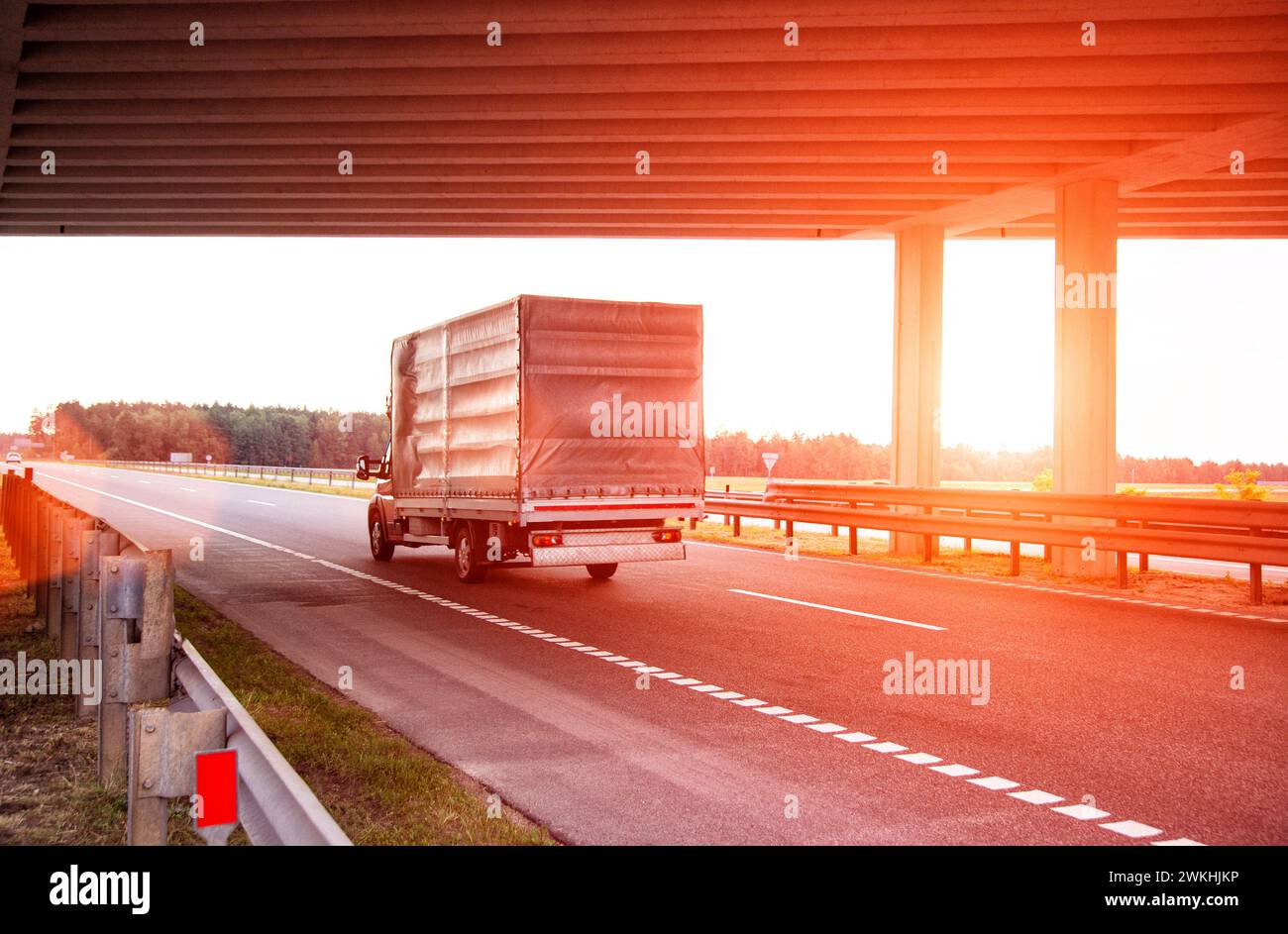 Une camionnette rouge transporte des appareils électroménagers vers une autre ville sur la route en été avec pour toile de fond le coucher du soleil. Logistique et affaires en c Banque D'Images