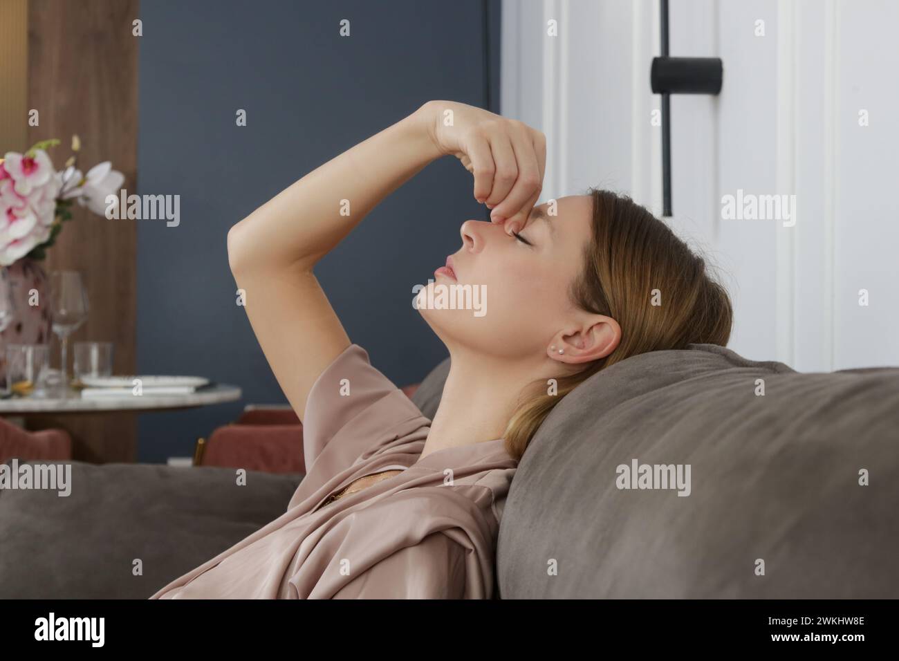 Vue latérale de la femme présentant des symptômes de sinusite frontale, sensation de pression entre les yeux assis sur le canapé dans le salon Banque D'Images