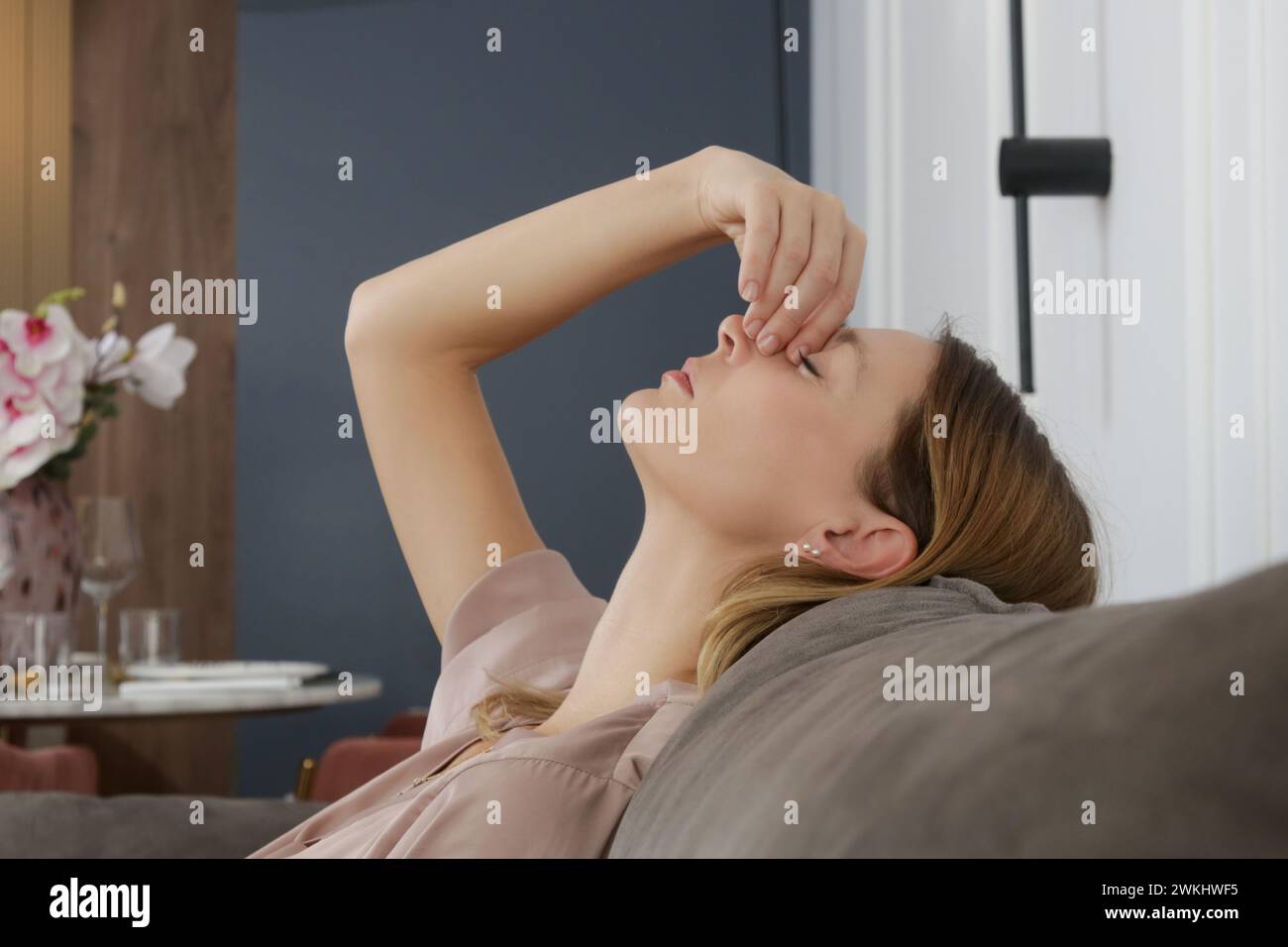 Vue latérale de la femme présentant des symptômes de sinusite frontale, sensation de pression entre les yeux assis sur le canapé dans le salon Banque D'Images