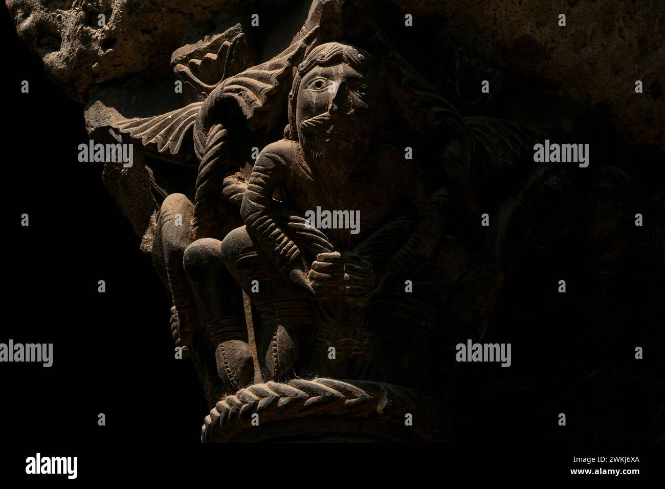 Homme regardant avec barbe de bouc, doigts proéminents sur les mains qu'il tient devant lui. Capitale romane de pierre sculptée Lombard dans le cloître au monastère de Santa Maria de Ripoll dans la province de Gérone, Catalogne, Espagne. Cette capitale se trouve au niveau inférieur plus tôt du cloître. Banque D'Images