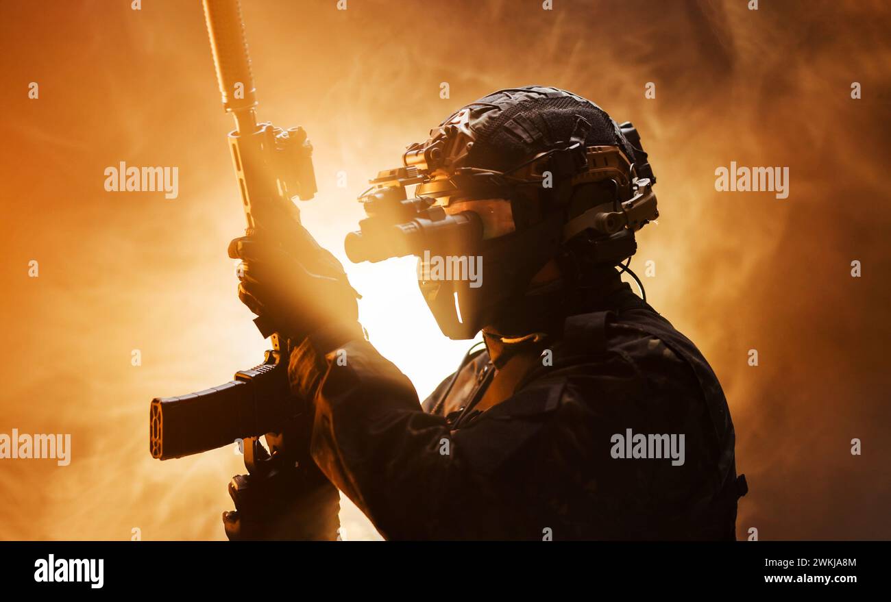 Homme concentré tenant une arme dans sa main d'une manière sérieuse. Soldat en tenue d'armée professionnelle complète contre fond de brouillard avec rétro-éclairage clignotant. Banque D'Images
