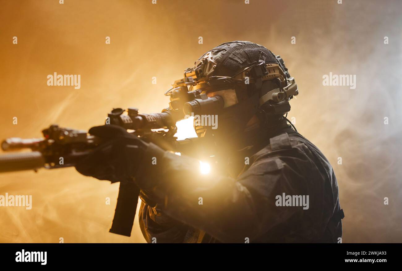 Homme concentré tenant une arme dans sa main d'une manière sérieuse. Soldat en tenue d'armée professionnelle complète contre fond de brouillard avec rétro-éclairage clignotant. Banque D'Images