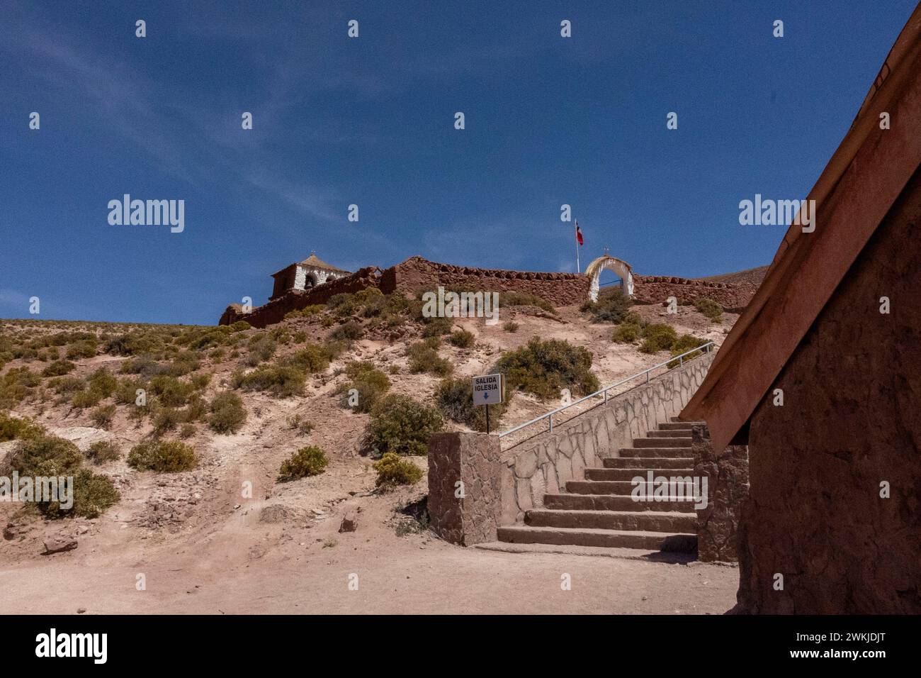 Escalier menant à la vieille église blanche dans le désert d'Atacama, Chili Amérique du Sud. Des escaliers mènent à une arche avec un drapeau volant. Banque D'Images