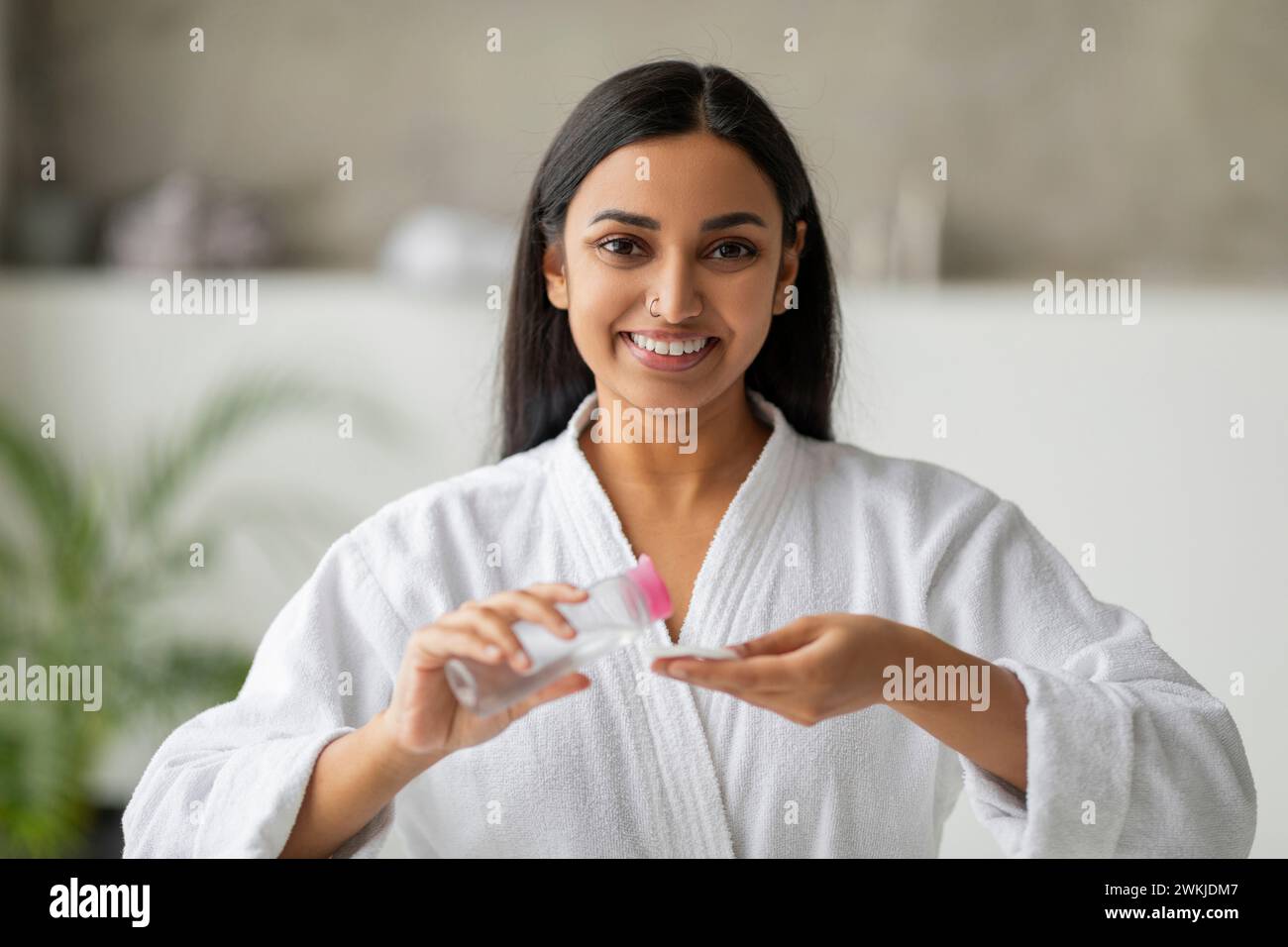 Positive jeune femme indienne nettoyant la peau hydratante dans la salle de bain Banque D'Images