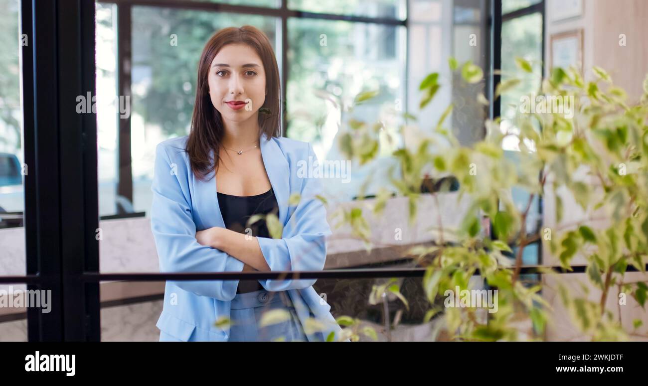 Belle femme d'affaires dans un bureau croisant les mains et regardant la caméra avec un sourire. Banque D'Images