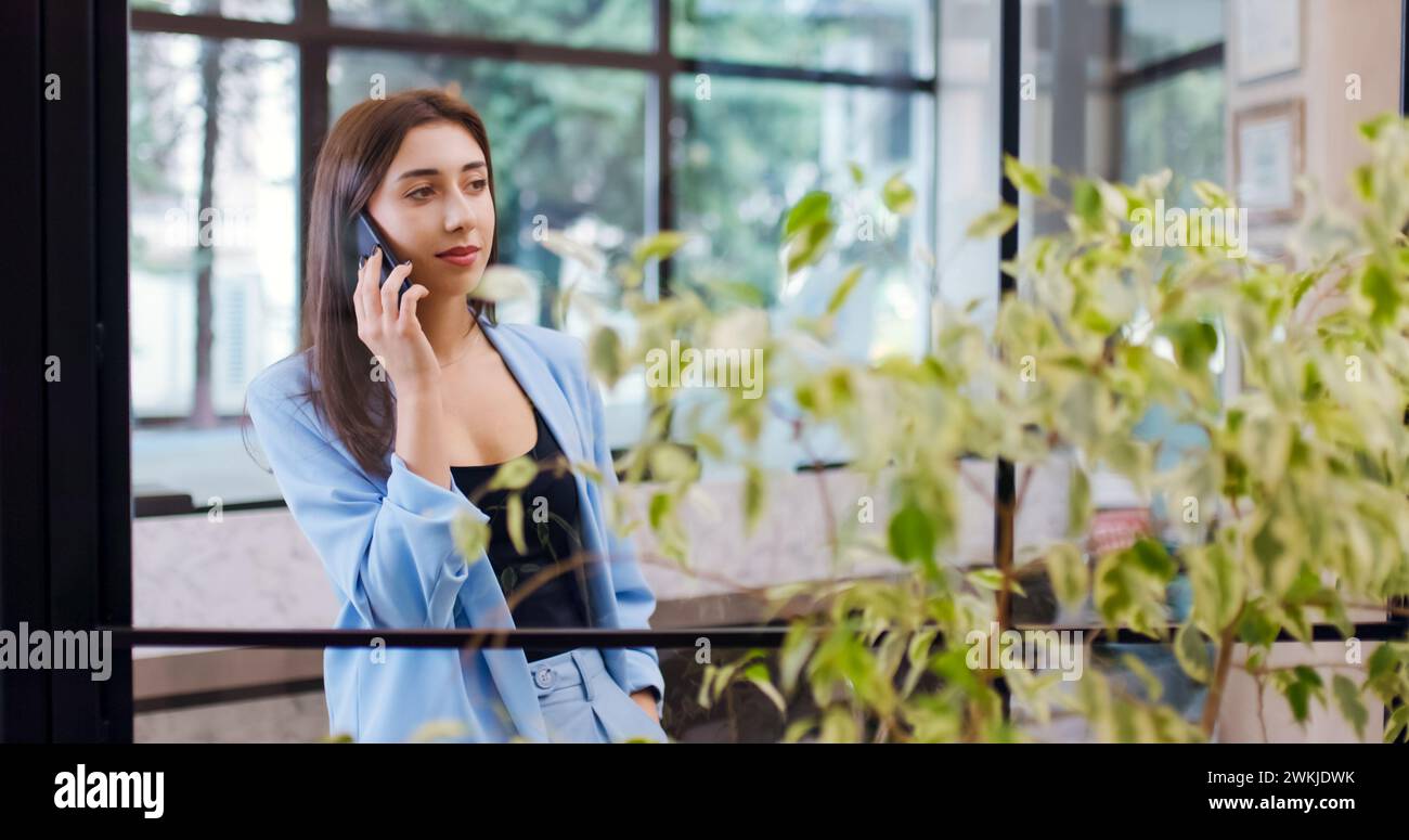 Belle femme d'affaires dans un bureau parlant au téléphone croisant les mains et regardant la caméra avec un sourire. Banque D'Images