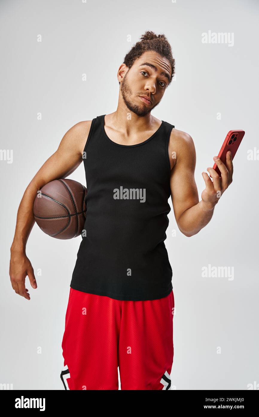 bel homme afro-américain tenant le basket-ball et le téléphone et regardant la caméra, paris en ligne Banque D'Images