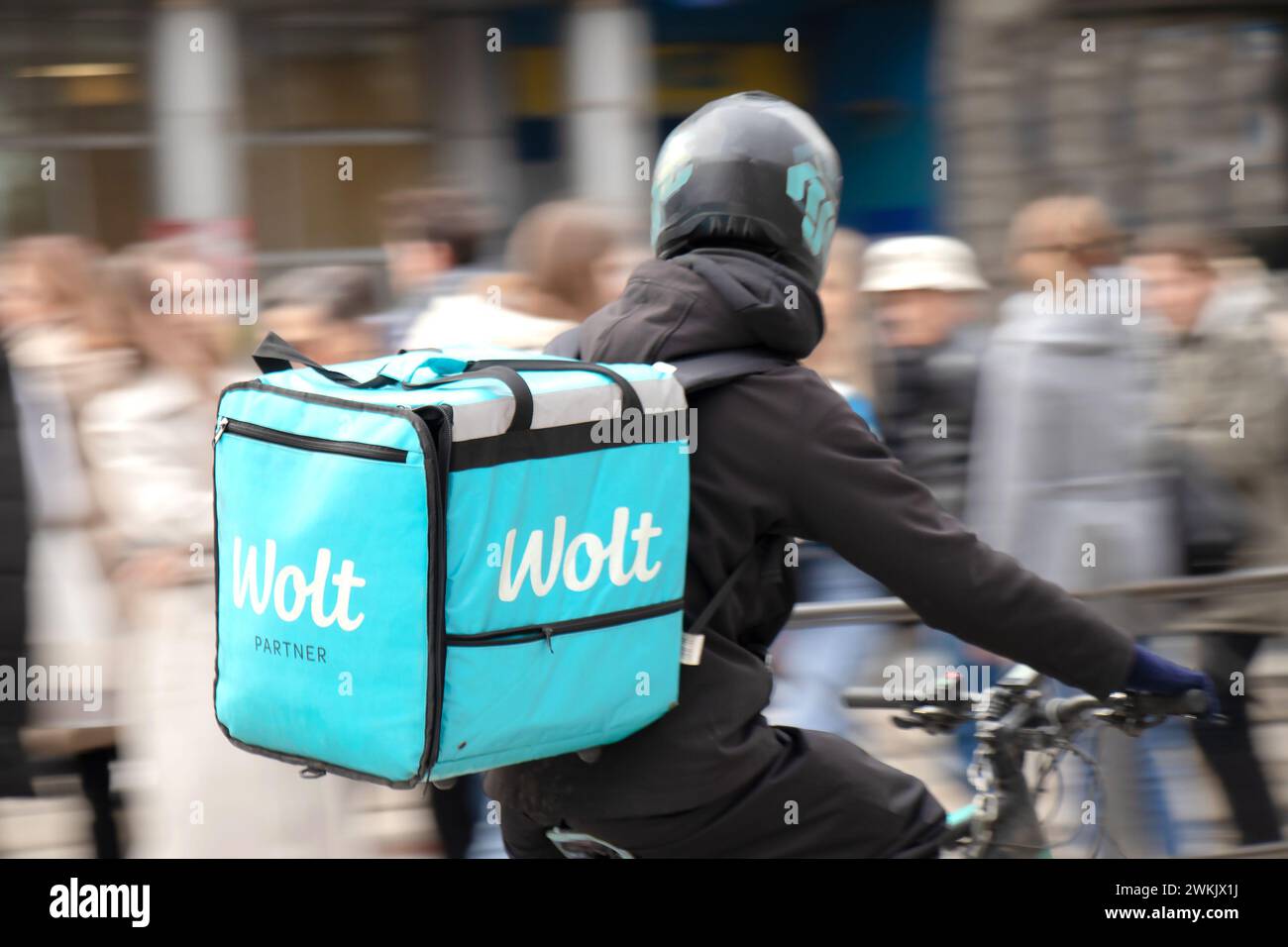 Belgrade, Serbie - 20 février 2024 : Wolt service courrier avec un sac de livraison vélo dans la rue animée de la ville pleine de piétons, vue arrière Banque D'Images