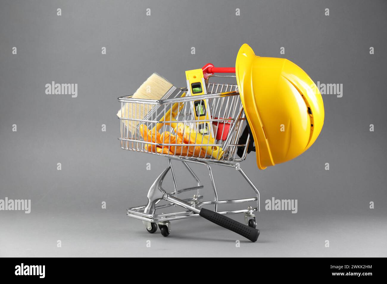 Petit chariot avec niveau de construction, brosse, gants et casque de sécurité sur fond gris Banque D'Images