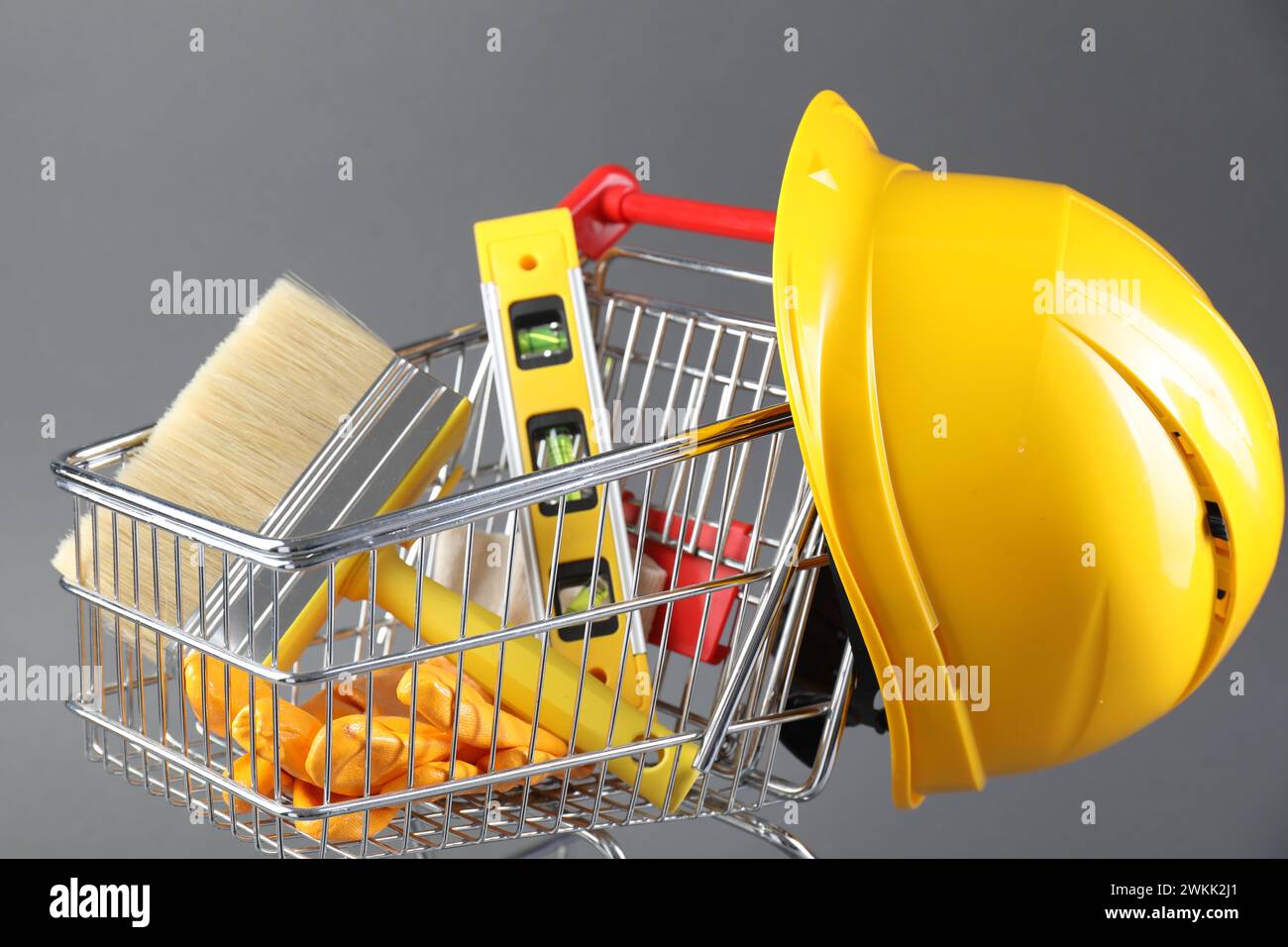 Petit chariot avec niveau de construction, brosse, gants et casque de sécurité sur fond gris Banque D'Images