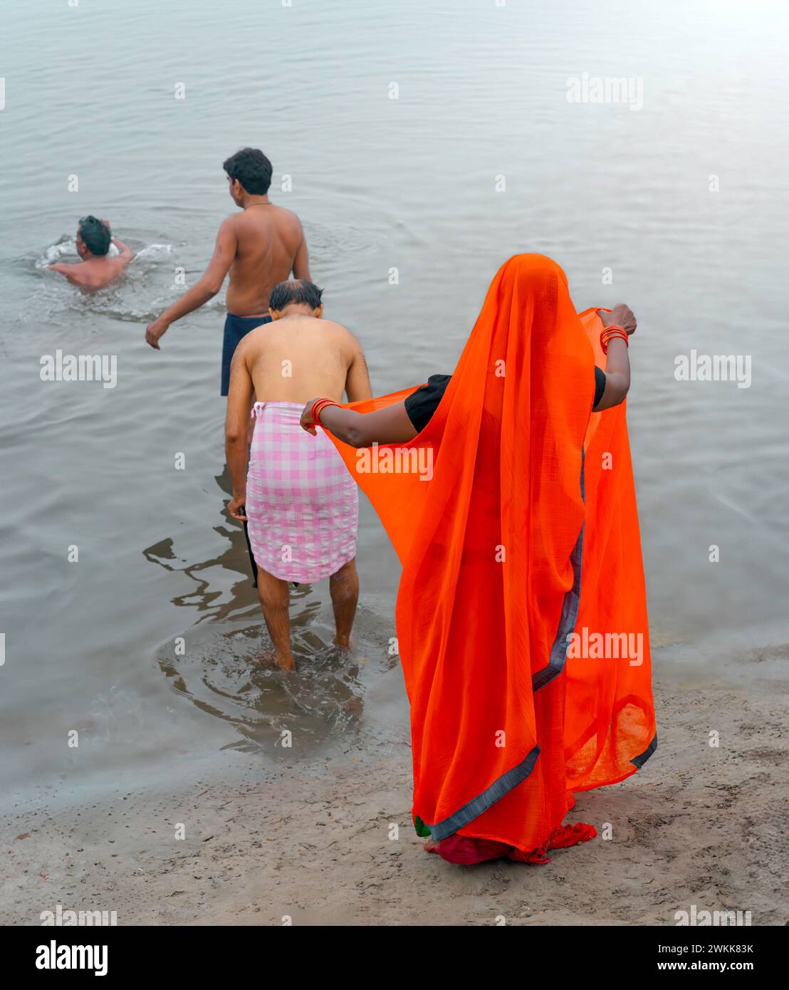 Femme dans le saree traditionnel et trois hommes prennent un bain rituel alors que l'aube se lève sur la rivière sainte Yamuna à Vrindavan, Royaume-Uni. Banque D'Images