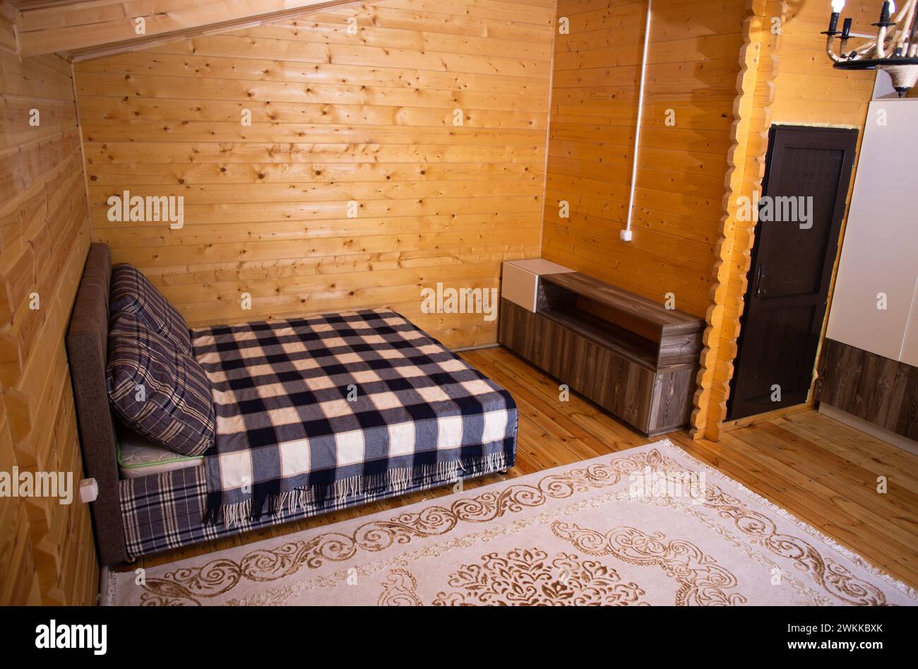 La chambre est décorée avec des lambris de bois chaleureux et un lit doux et accueillant. Un beau lustre fournit un éclairage doux. Banque D'Images