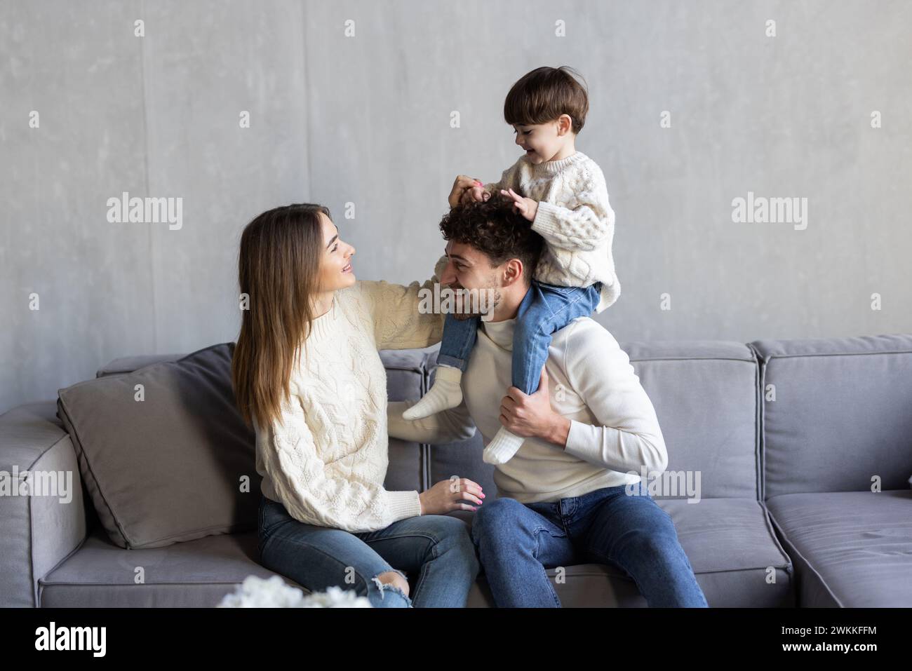 Heureux jeune famille caucasienne avec petit fils de 7s se détendre sur le canapé dans le salon utiliser un smartphone moderne ensemble. Des parents souriants avec un petit garçon parlent Banque D'Images