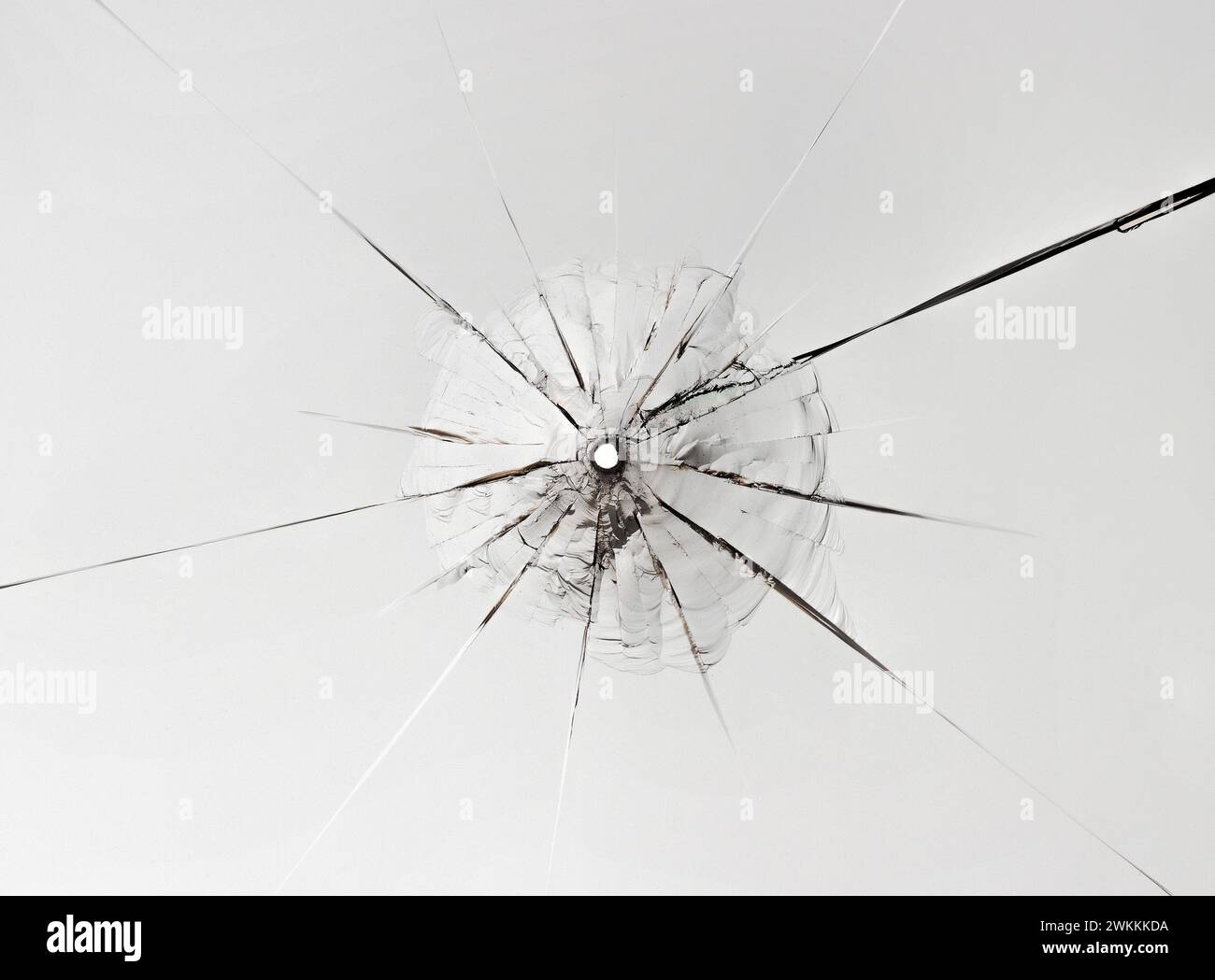 Petit trou dans le verre avec de longues fissures sur fond blanc. Gros plan. Banque D'Images