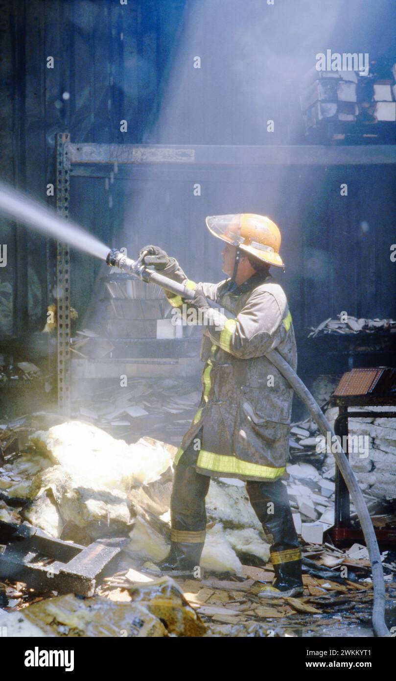Un puits de lumière provenant d'un trou dans le toit éclaire un pompier tirant un jet d'eau provenant d'un tuyau d'incendie tout en éteignant le feu à l'entrepôt. ©Bob Daemmrich Banque D'Images