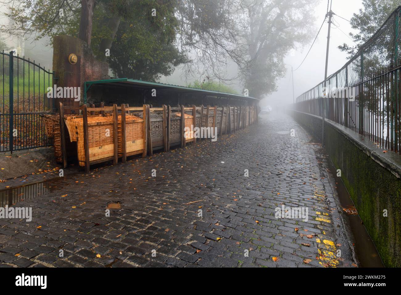 Luge en osier luge en rangées contre un mur le long des rues pavées humides lors d'une journée brumeuse pluvieuse dans le quartier Monte de Funchal Madeira Portugul Banque D'Images