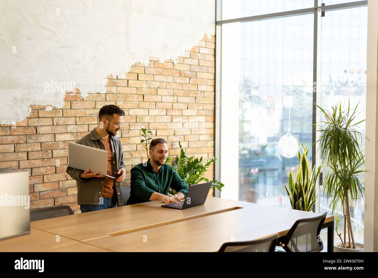 Deux professionnels souriants s’engagent dans une séance de travail collaboratif à une table en bois, leur camaraderie évidente dans un cadre de bureau contemporain avec un Banque D'Images