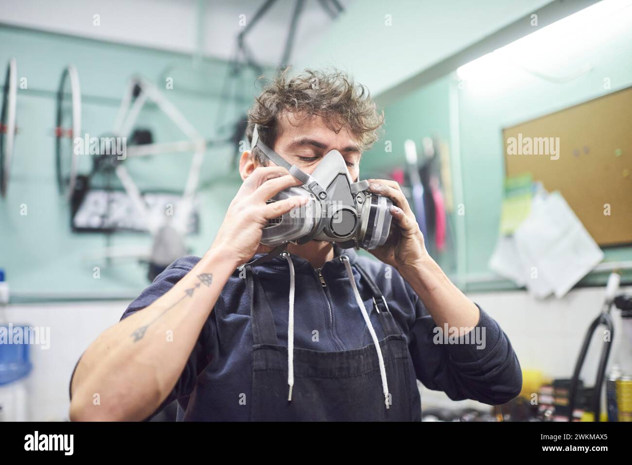 Jeune travailleur latin enlevant un masque de protection respiratoire, alors qu'il termine un travail de peinture au pistolet dans son atelier. Protection de la santé dans l'industrie Banque D'Images