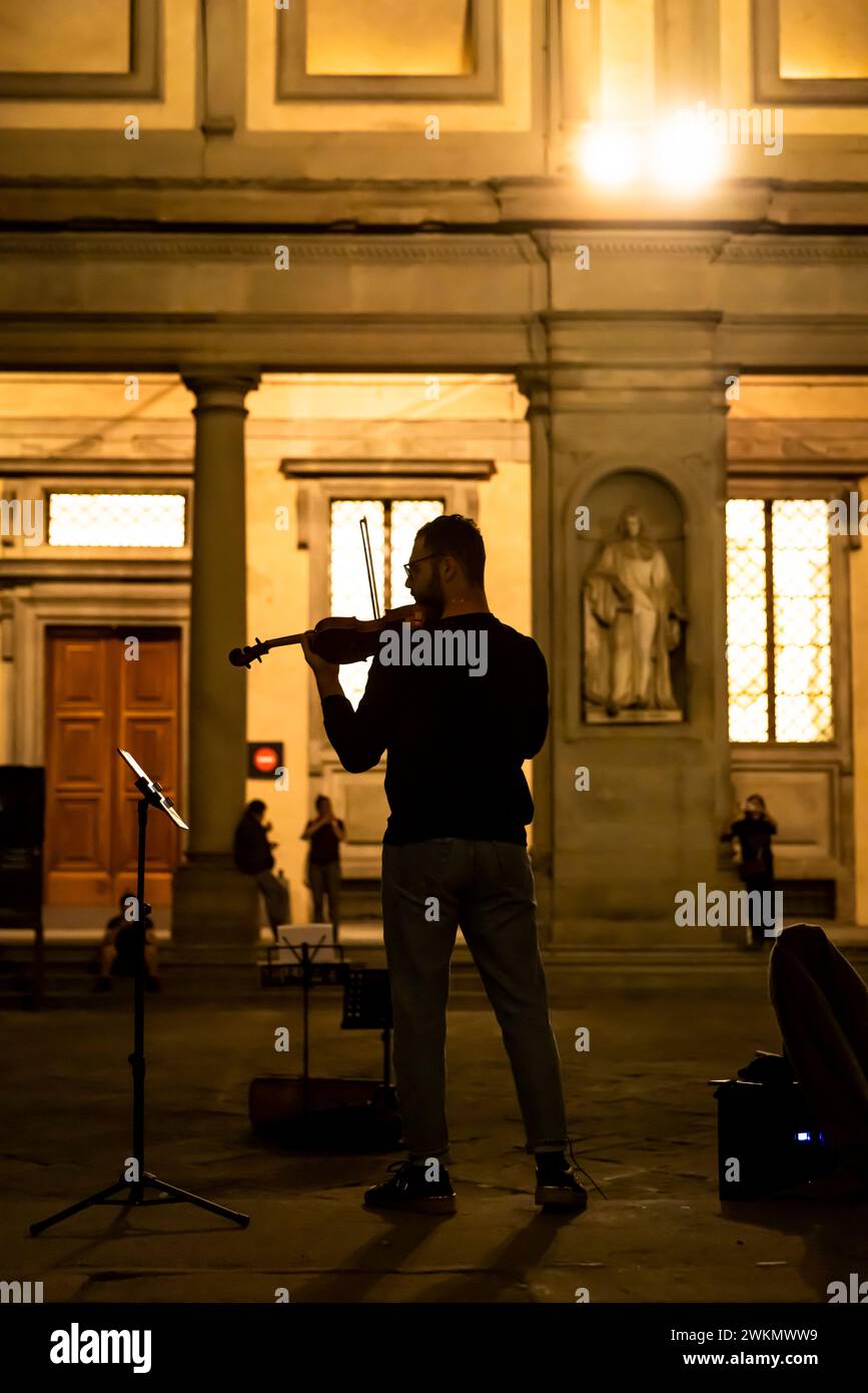 Le busking en Italie est une tradition honorée par le temps où les musiciens jouent dans les rues pour obtenir des conseils. Un homme joue du violon la nuit près de la Galerie des Offices. Banque D'Images