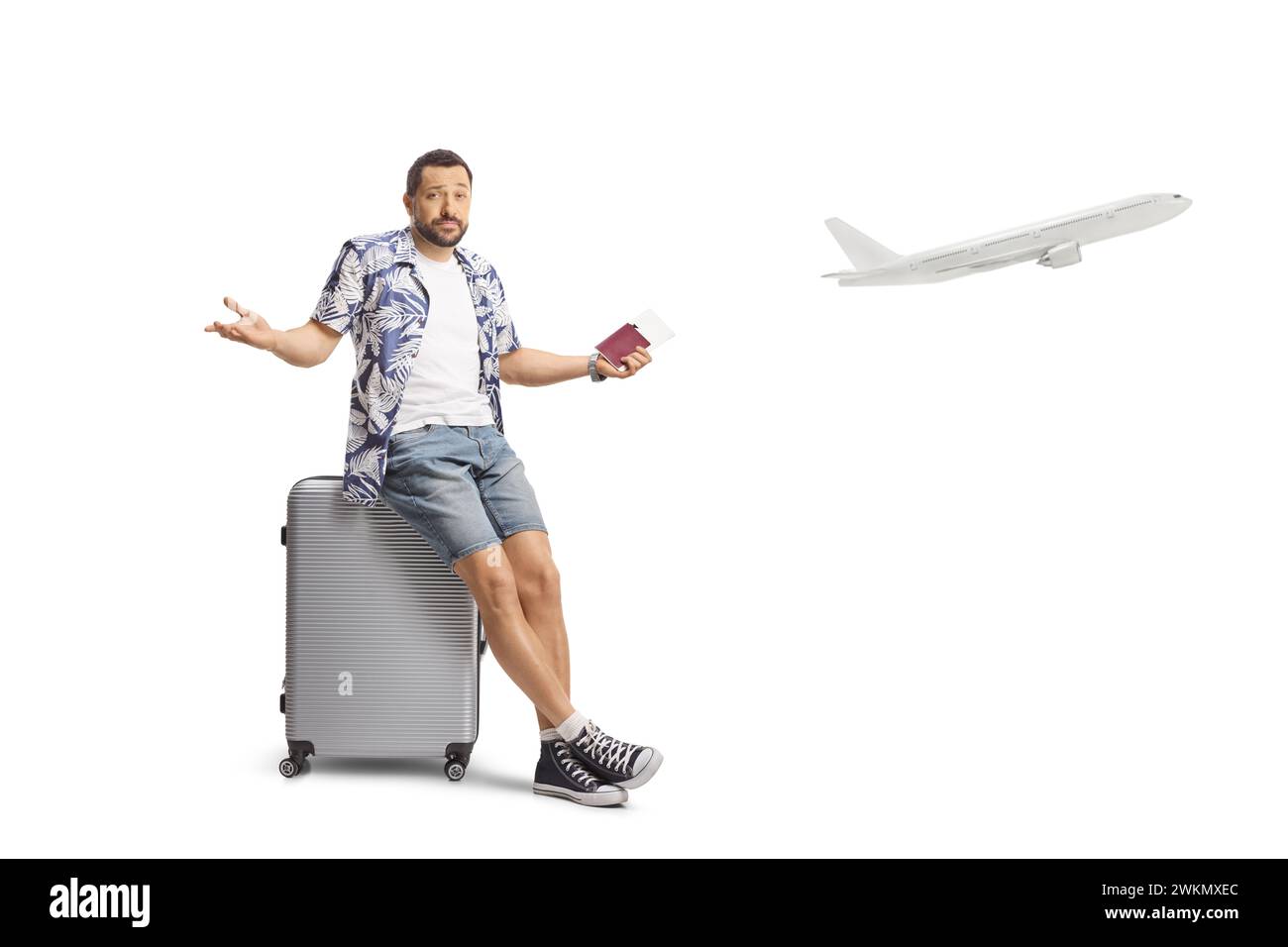 Homme confus tenant un passeport et assis sur une valise attendant un vol retardé isolé sur fond blanc Banque D'Images