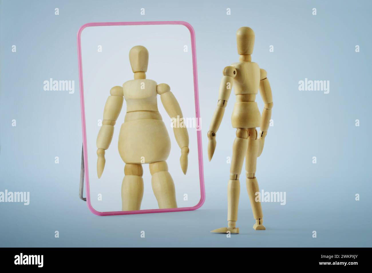 Mannequin en bois mince regardant dans le miroir et se voyant comme graisse - anorexie et troubles alimentaires concept Banque D'Images