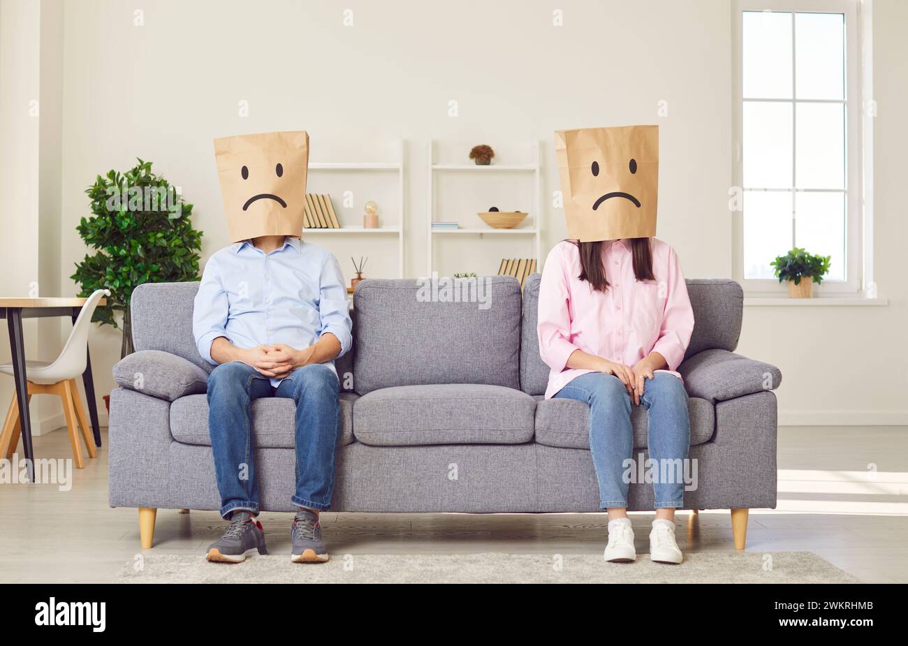 Couple assis sur les côtés opposés du canapé avec des sacs en papier avec des visages bouleversés ignorant l'un l'autre. Banque D'Images