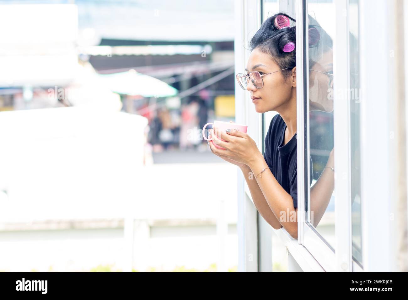 Une jeune femme tient une tasse dans une fenêtre ouverte d'un immeuble Banque D'Images