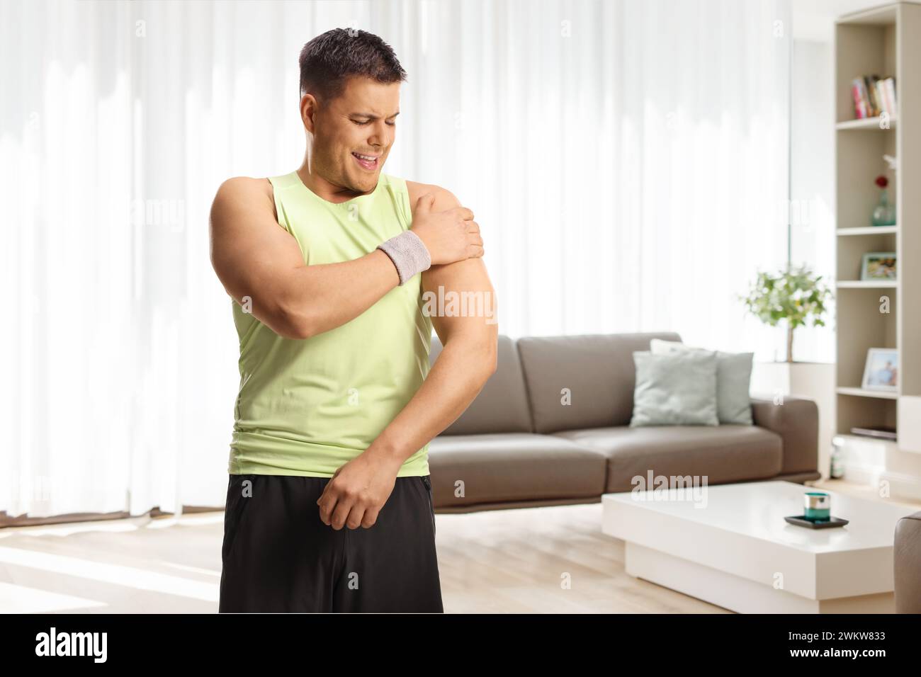 Homme en vêtements de sport tenant son épaule à la maison, douleur et problèmes de santé Banque D'Images