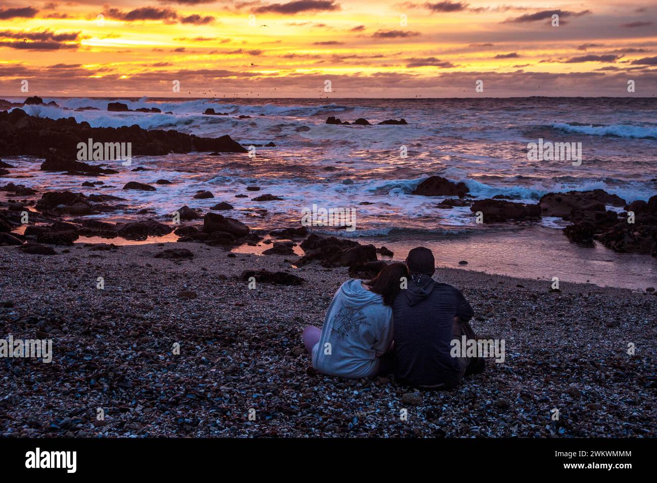 Couple sitting on beach at sunset Banque D'Images