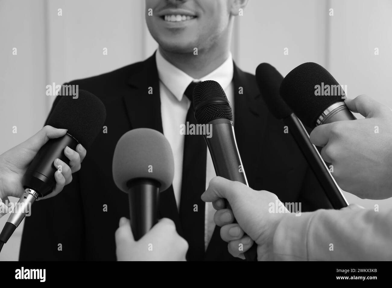 Homme d'affaires donnant une interview à des journalistes à l'intérieur, gros plan. Effet noir et blanc Banque D'Images