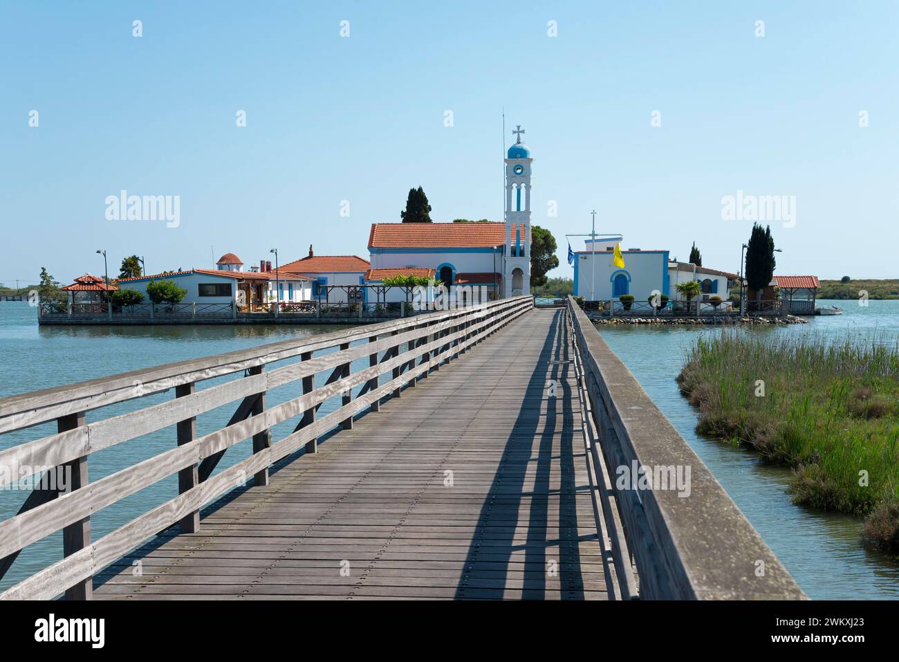 Une passerelle en bois mène au-dessus des eaux calmes à un monastère sous un ciel bleu clair, monastère de Saint Nicolas, monastère d'Agios Nikolaos, Agiou Nikolao Banque D'Images