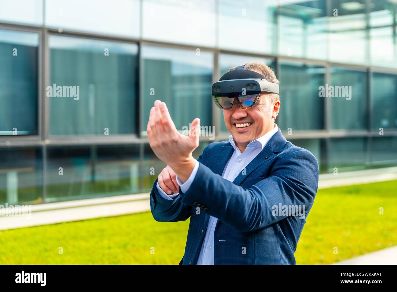 Homme d'affaires caucasien adulte heureux souriant tout en portant des lunettes de réalité mixte à l'extérieur d'un bâtiment financier Banque D'Images