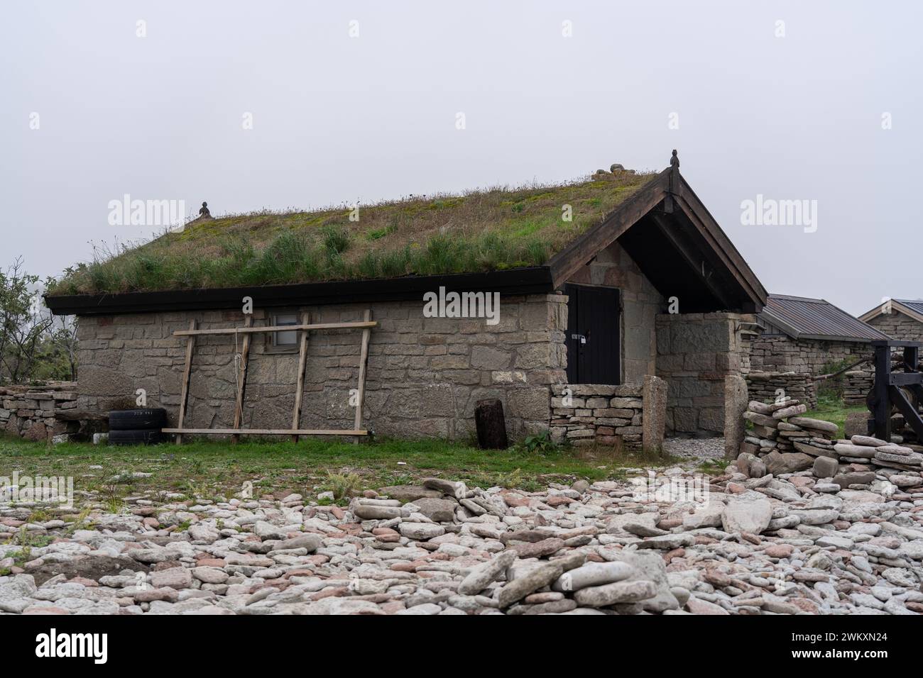Un petit bâtiment en pierre avec un toit vert luxuriant, entouré de rochers au premier plan Banque D'Images