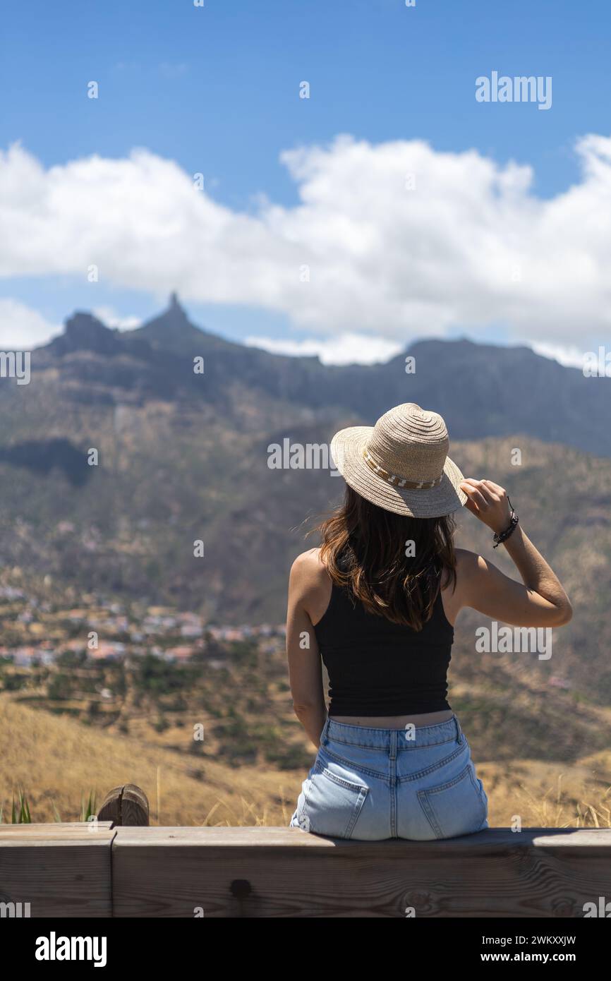 Vue arrière d'une jeune femme avec un chapeau assis regardant la majestueuse Roque Nublo à Gran Canaria, îles Canaries, Espagne Banque D'Images