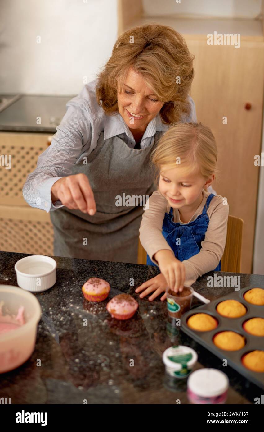 Grand-mère, enfant et cuisson de cupcakes ou de saupoudrées de décorations glaçantes ou apprentissage de la créativité, de la liaison ou du travail d'équipe. Personne féminine, fille et douce Banque D'Images