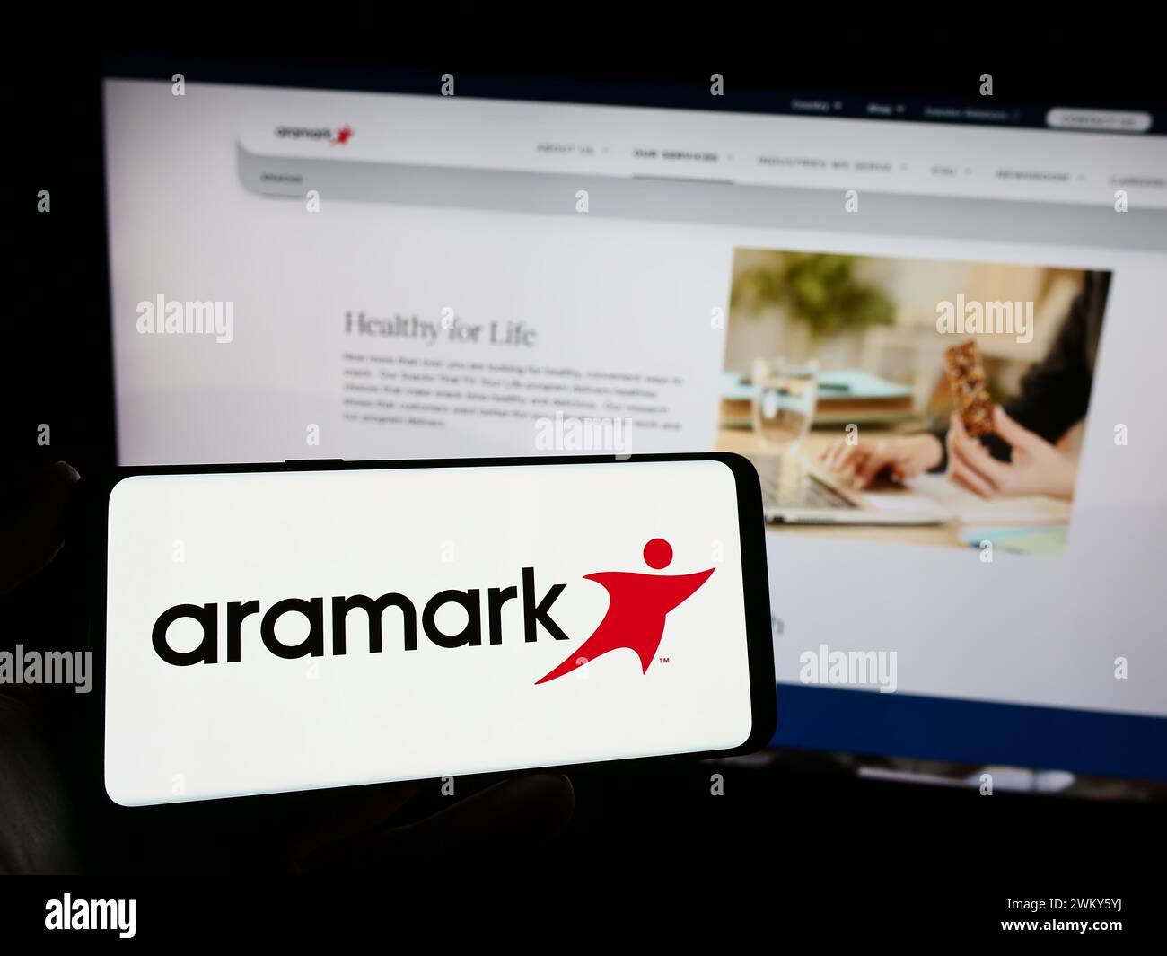 Personne tenant le téléphone portable avec le logo de la société américaine de services alimentaires et de gestion des installations Aramark en face de la page Web. Concentrez-vous sur l'affichage du téléphone. Banque D'Images