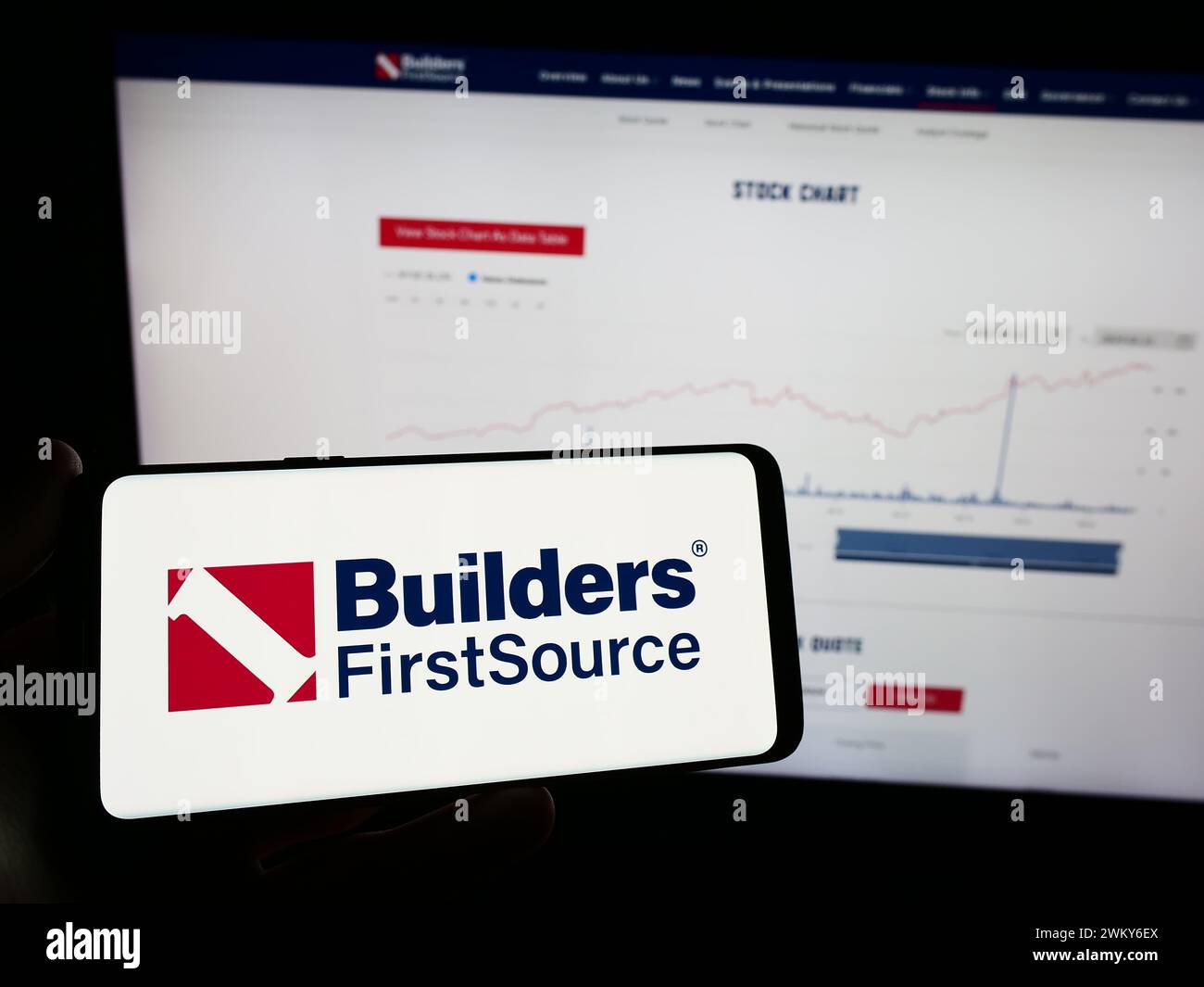Personne tenant le téléphone portable avec le logo de la société américaine de matériaux de construction Builders FirstSource Inc en face de la page Web. Concentrez-vous sur l'affichage du téléphone. Banque D'Images