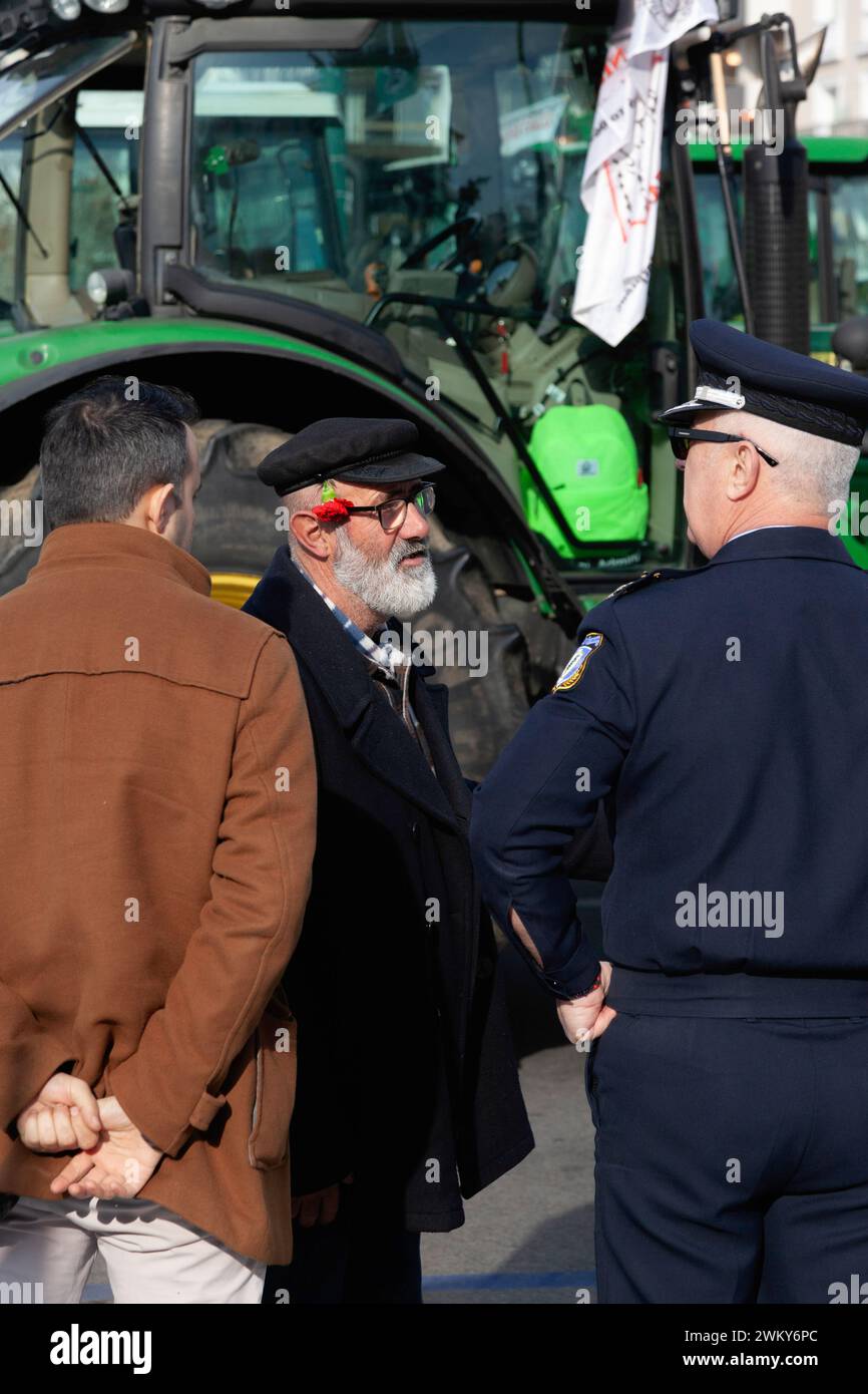 Un vieil homme avec une barbe blanche, une casquette noire et une fleur d'oeillet à l'arrière de l'oreille parle à un homme et à un policier lors d'une manifestation Banque D'Images