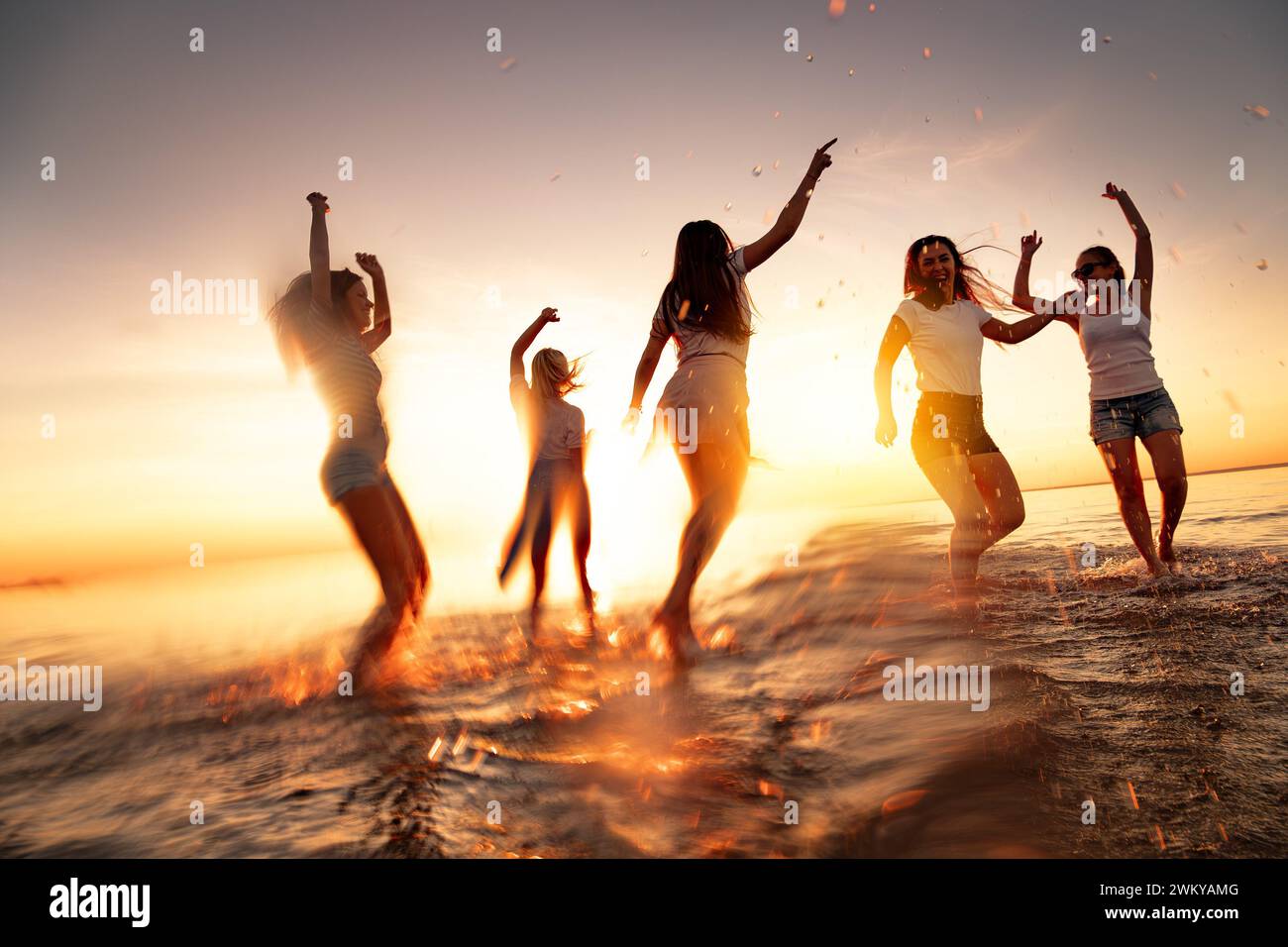 Groupe de jeunes filles heureuses s'amusent et dansent à la plage calme du coucher du soleil. Mouvement flou Banque D'Images
