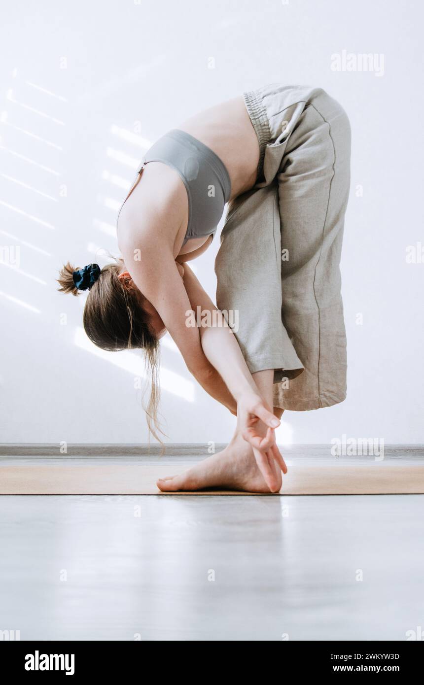 Femme en pantalon en lin faisant la pose de pliage avant de yoga créatif Banque D'Images
