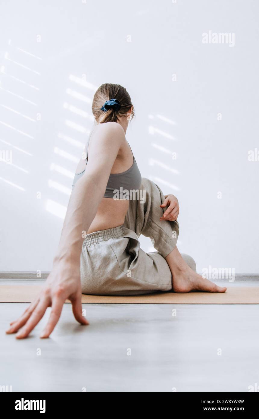 Femme dans un pantalon en lin naturel faisant une pose de yoga twist assis sur un tapis de liège Banque D'Images
