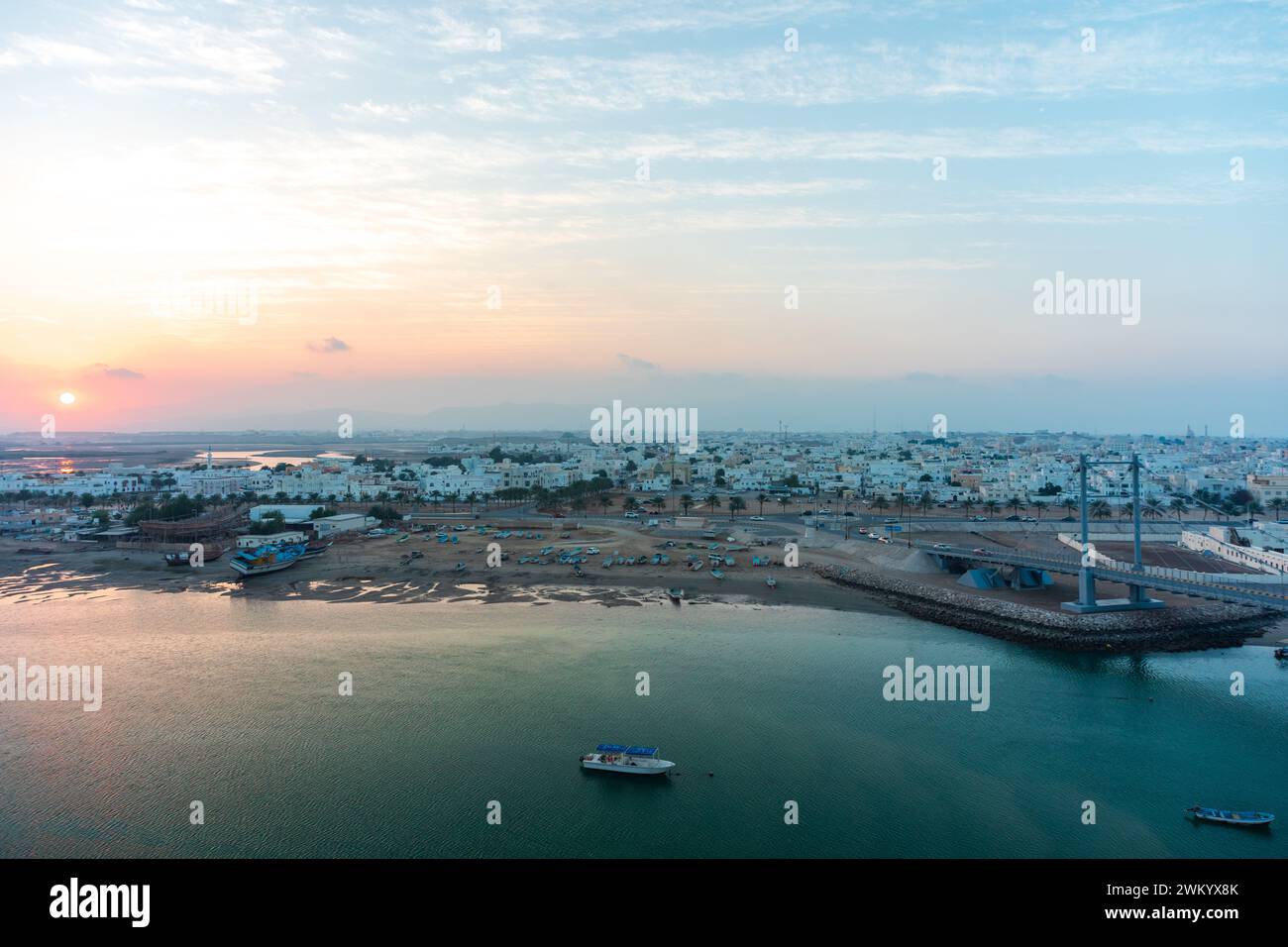 Coucher de soleil dans la ville de sur. Vue sur la partie ouest de la ville sur. Facteur dhow en distance. Sur, Oman Banque D'Images