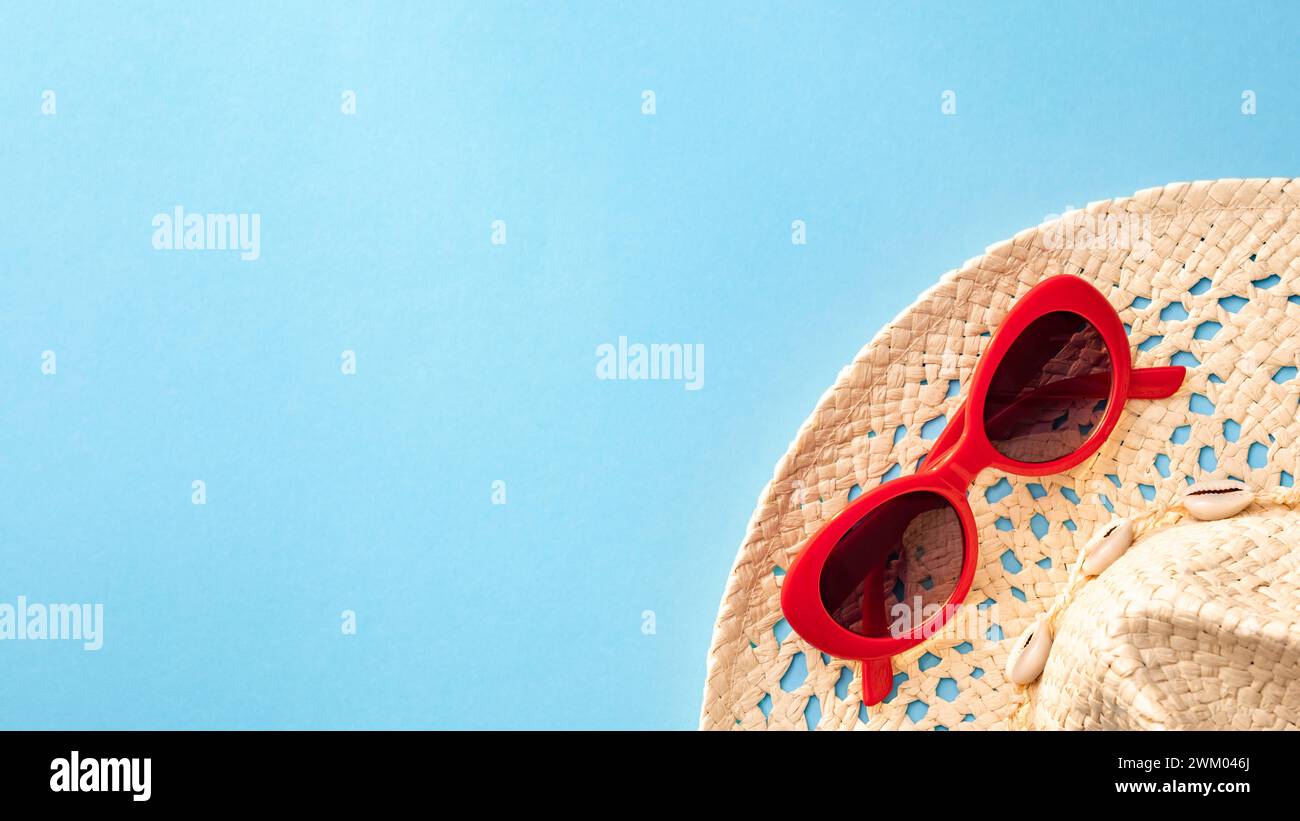 Chapeau de paille avec lunettes de soleil rouges sur un fond bleu en été Banque D'Images