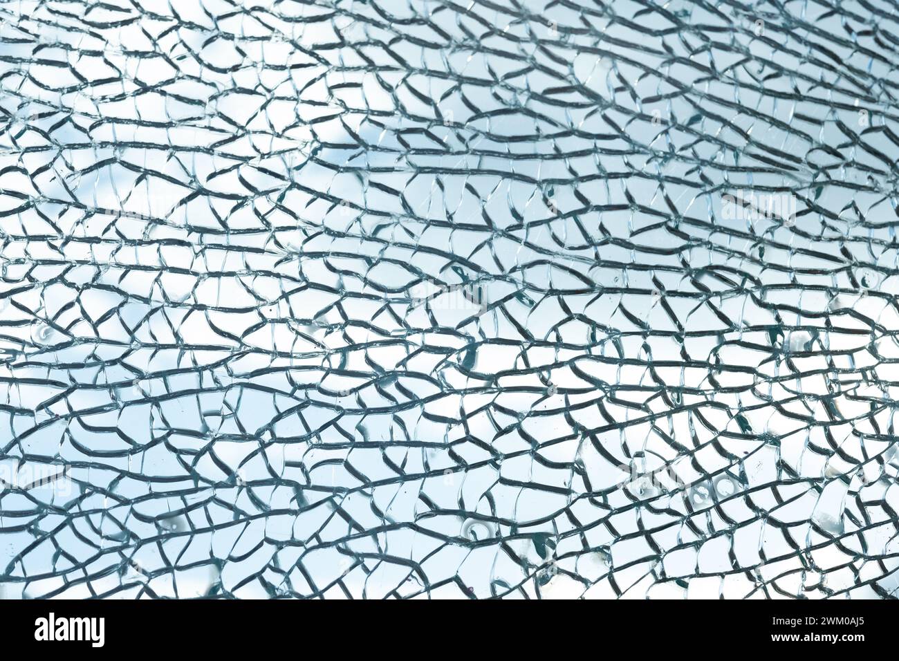 Des motifs complexes se forment dans le verre brisé, créant une toile complexe de fissures. Les fragments translucides reflètent la lumière, mettant en valeur une beauté délicate mais chaotique. La texture du verre brisé sur un fond de ciel bleu. Banque D'Images